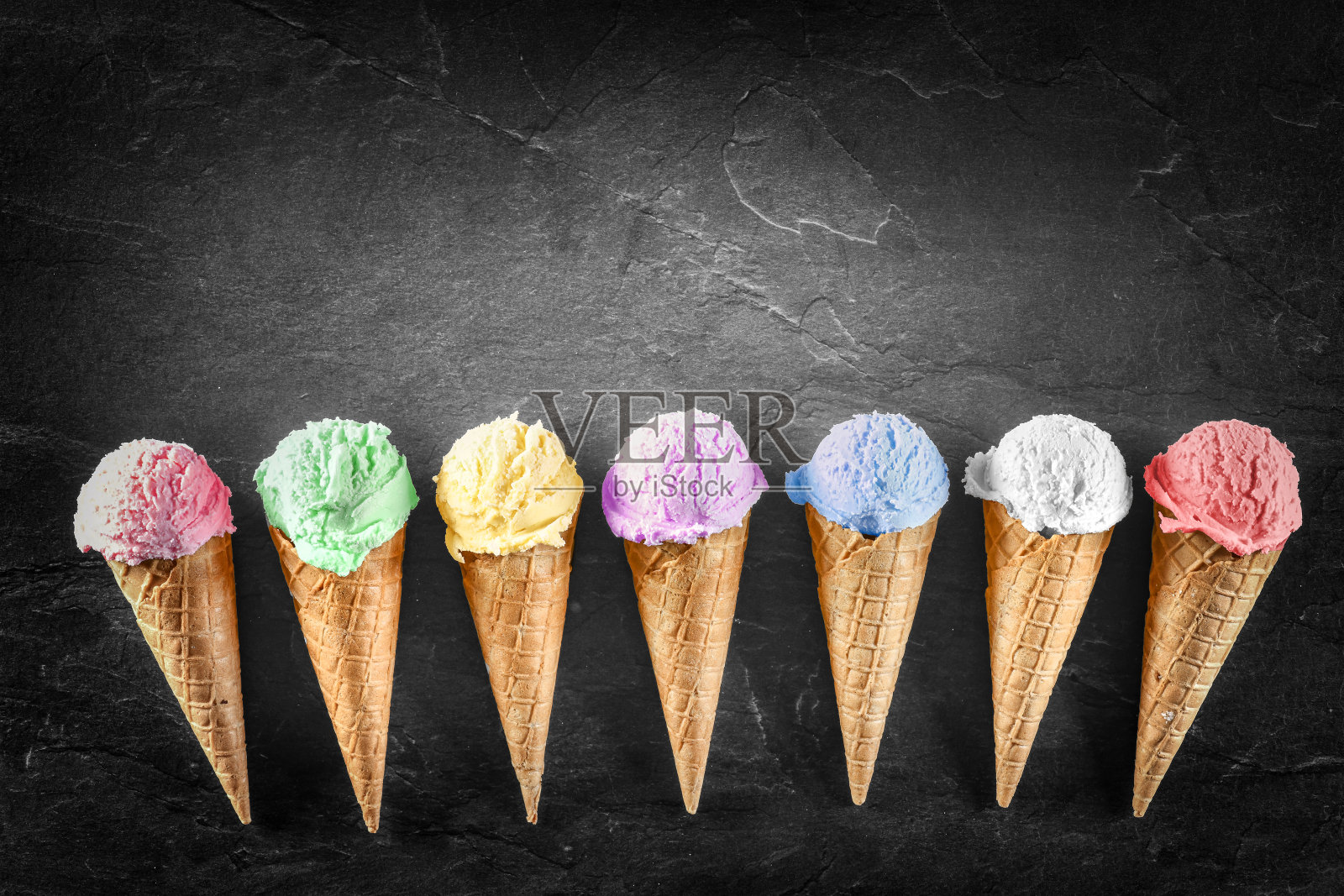 在黑色背景上排列成一排的锥形冰淇淋球。五颜六色的不同口味的冰淇淋球。巧克力、柠檬、青柠、杏仁、草莓等甜冰淇淋照片摄影图片