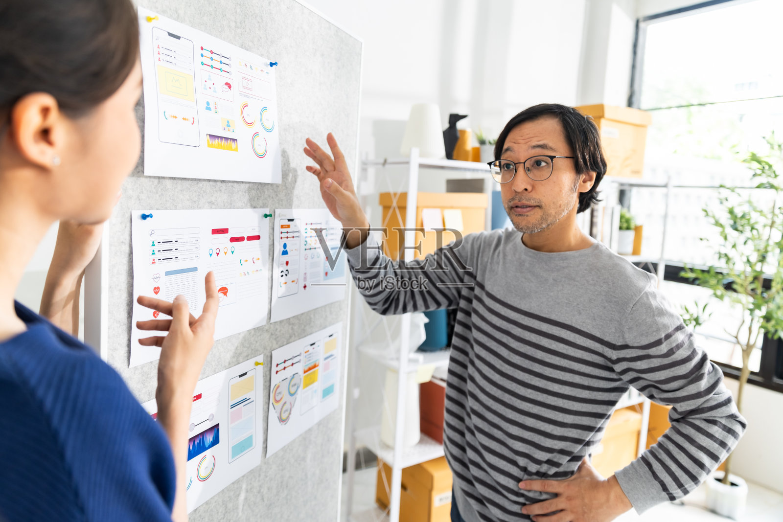 两个富有创意的亚洲人在创意办公室分享想法并讨论移动应用程序界面设计。照片摄影图片