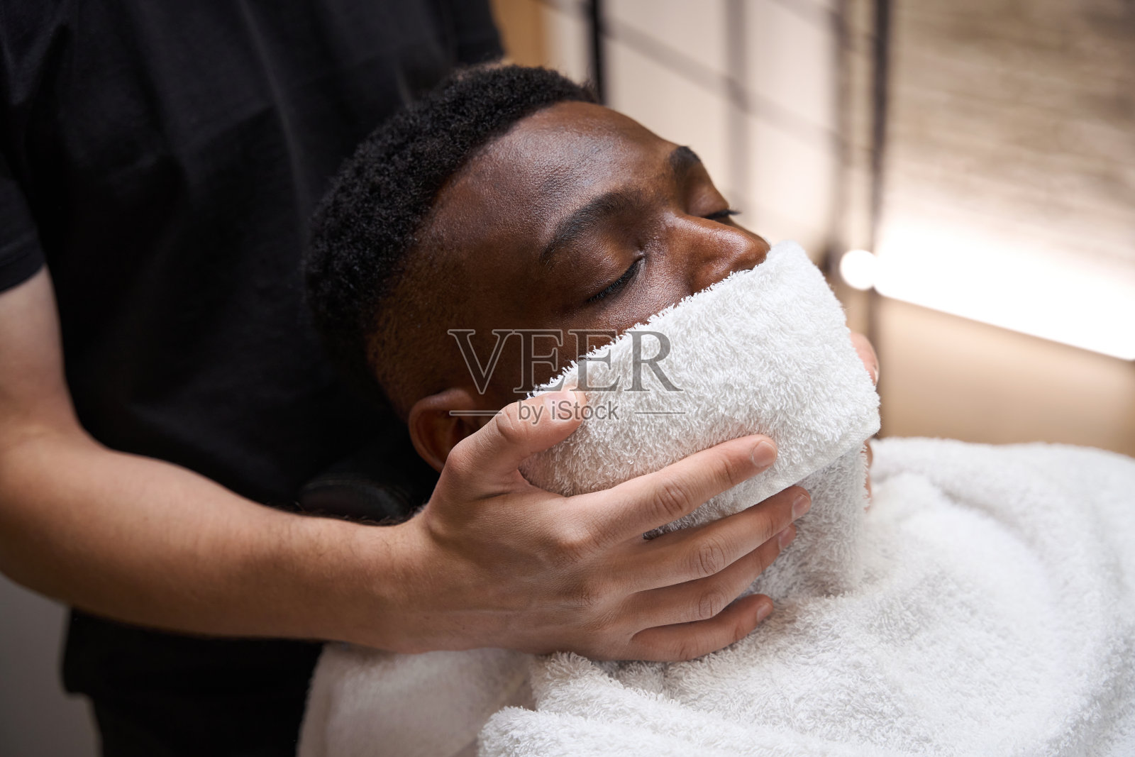 理发师把热毛巾放在非裔美国人的脸上照片摄影图片