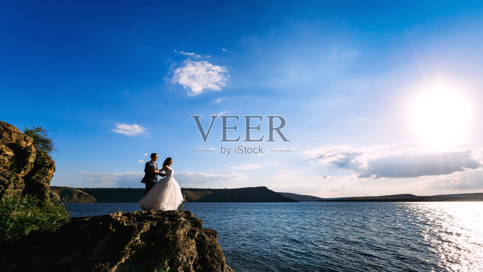 美丽的新婚夫妇站在平静的大海和岩石上照片摄影图片