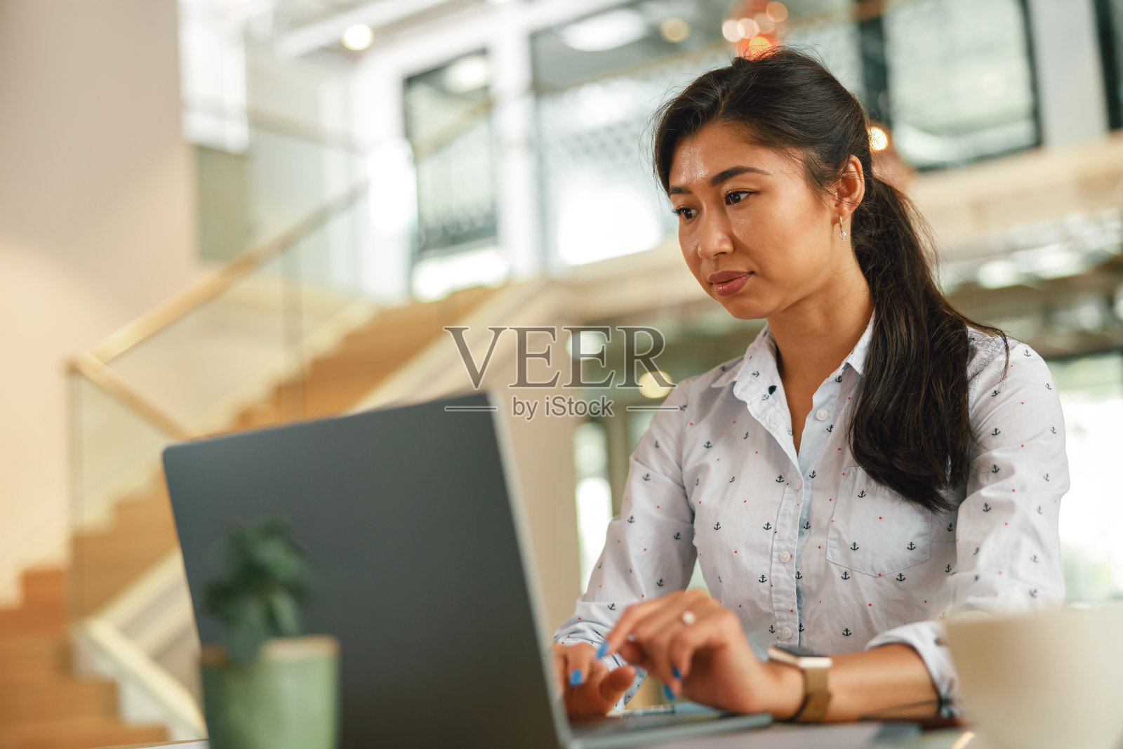 专注时尚的商务女性坐在办公室背景的桌子上用笔记本电脑工作照片摄影图片