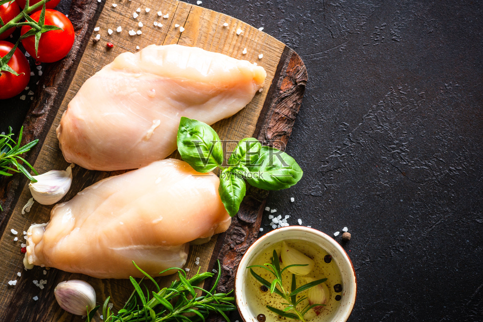 黑色餐桌上的木板上放着香料和蔬菜的鸡胸肉。照片摄影图片