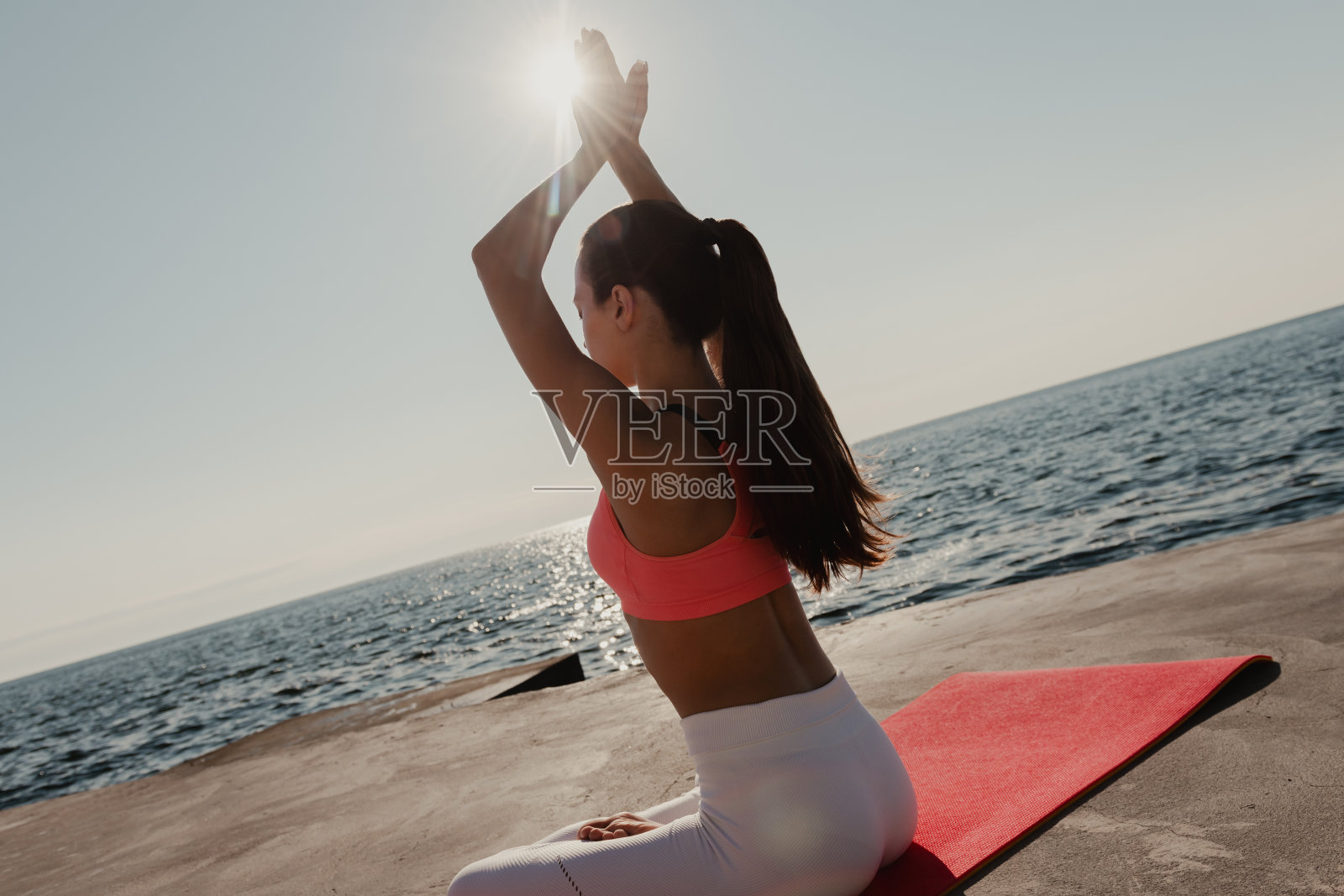 身穿运动服的女子在海边以莲花坐姿练习瑜伽的后视图照片摄影图片