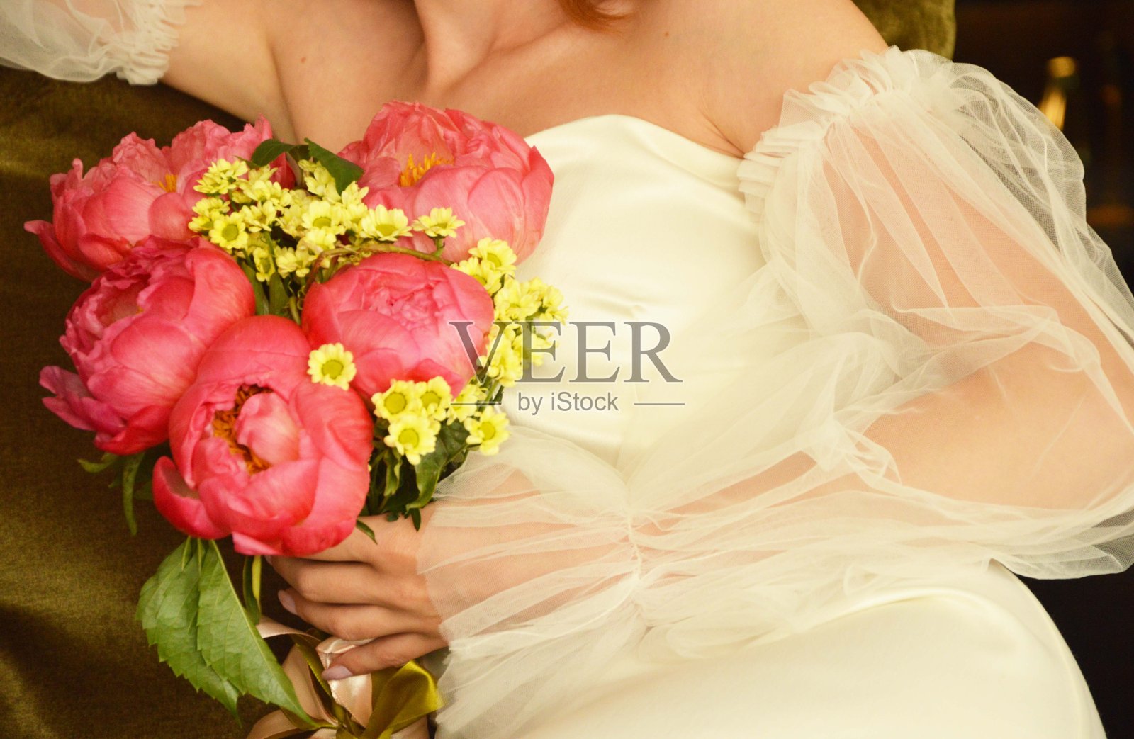 身着白色礼服的新娘手里捧着一束鲜艳的结婚牡丹。照片摄影图片