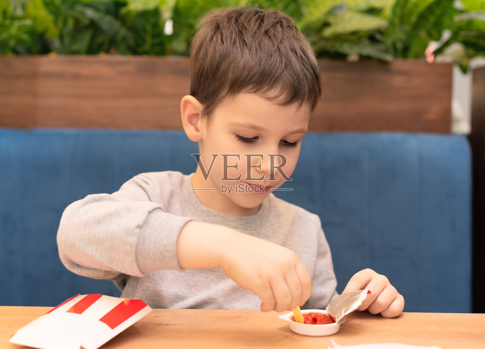 一个小男孩在咖啡馆里蘸着番茄酱吃炸薯条。垃圾食品，不健康的饮食观念照片摄影图片