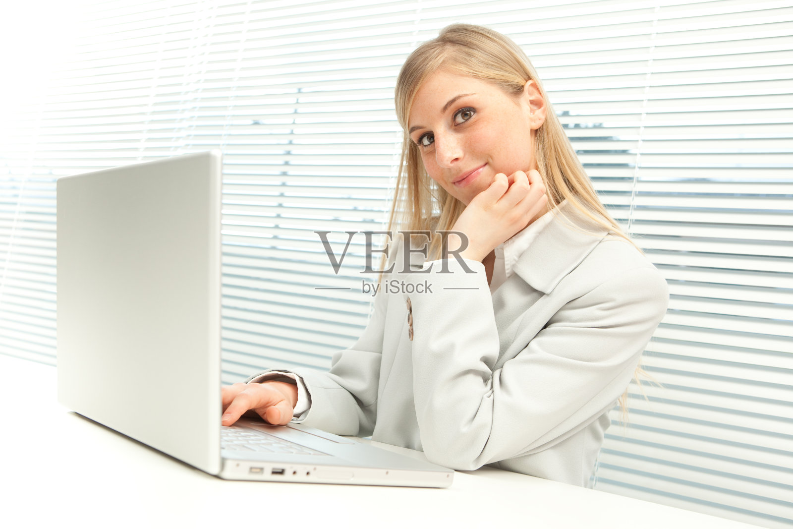 带着笔记本电脑微笑的金发商务女孩靠近百叶窗照片摄影图片