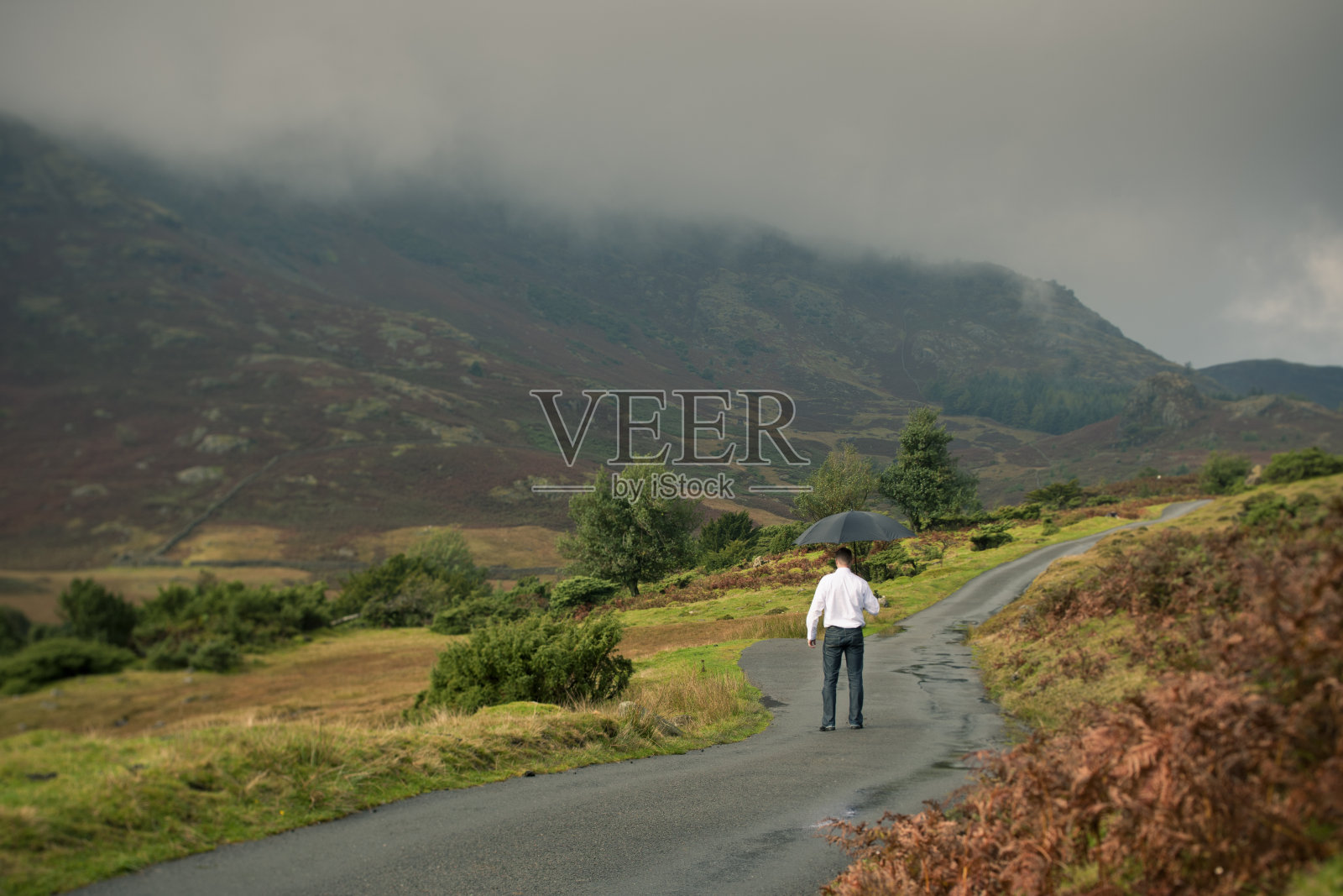 弯弯曲曲的乡村小路上，拿着雨伞的男人照片摄影图片