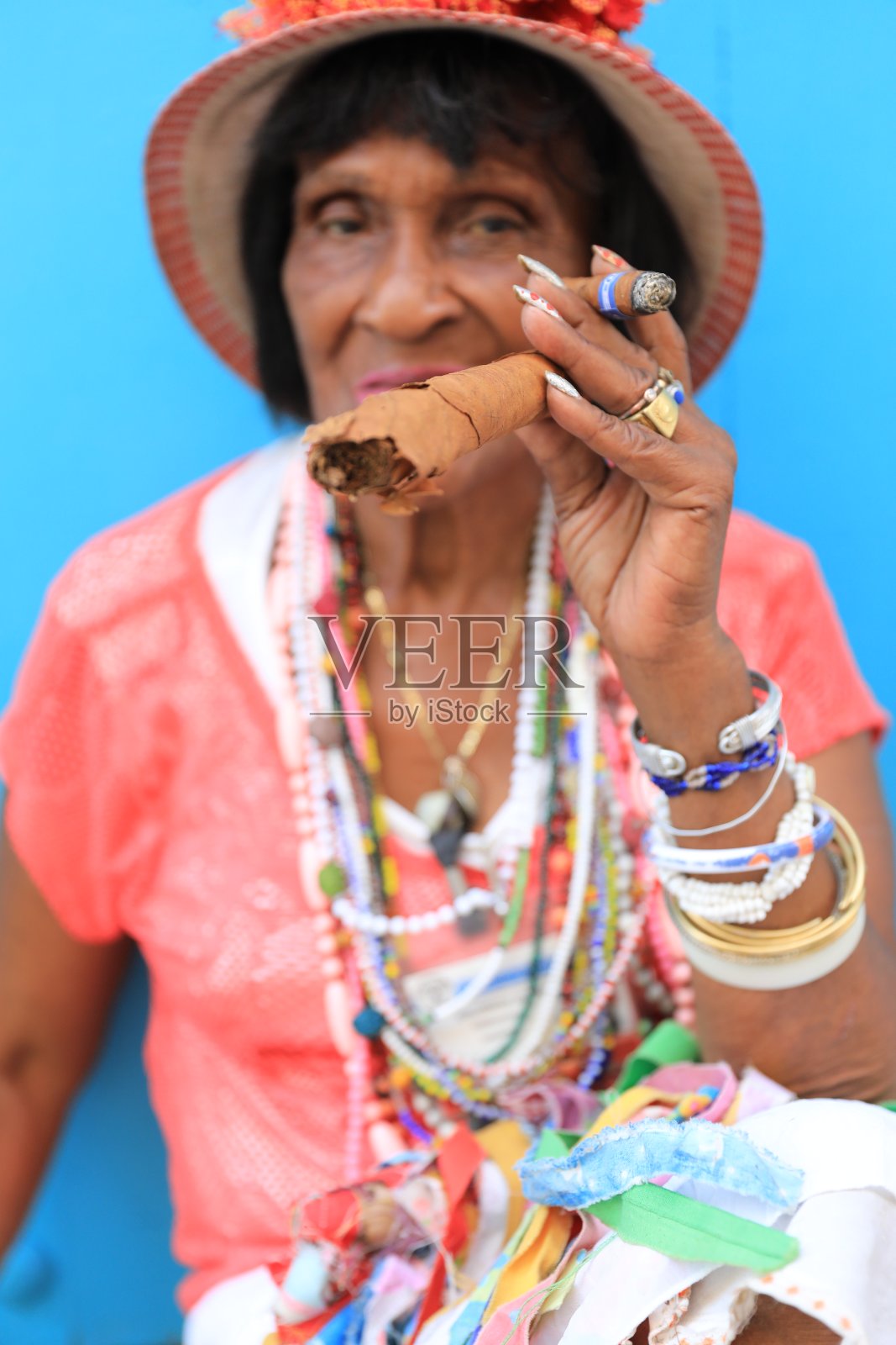 在古巴哈瓦那，一位传统的古巴老妇手拿雪茄站在蓝色的墙前照片摄影图片