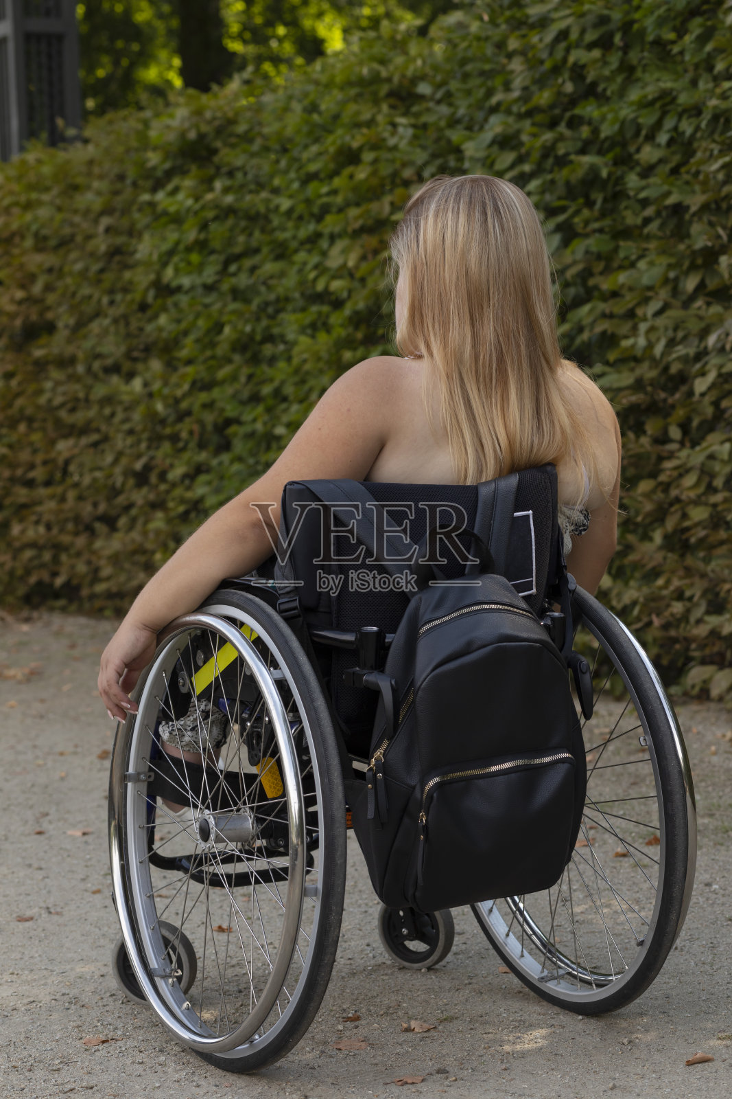 夏日，坐在轮椅上的矮个儿年轻女子在绿色公园里享受时光。成年残疾女性全身后视图。孤独和悲伤的概念。垂直平面照片摄影图片
