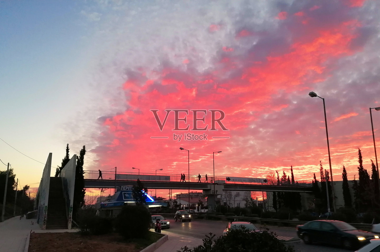 人们正走在人行天桥上，远处天空中有一片红云形成。照片摄影图片