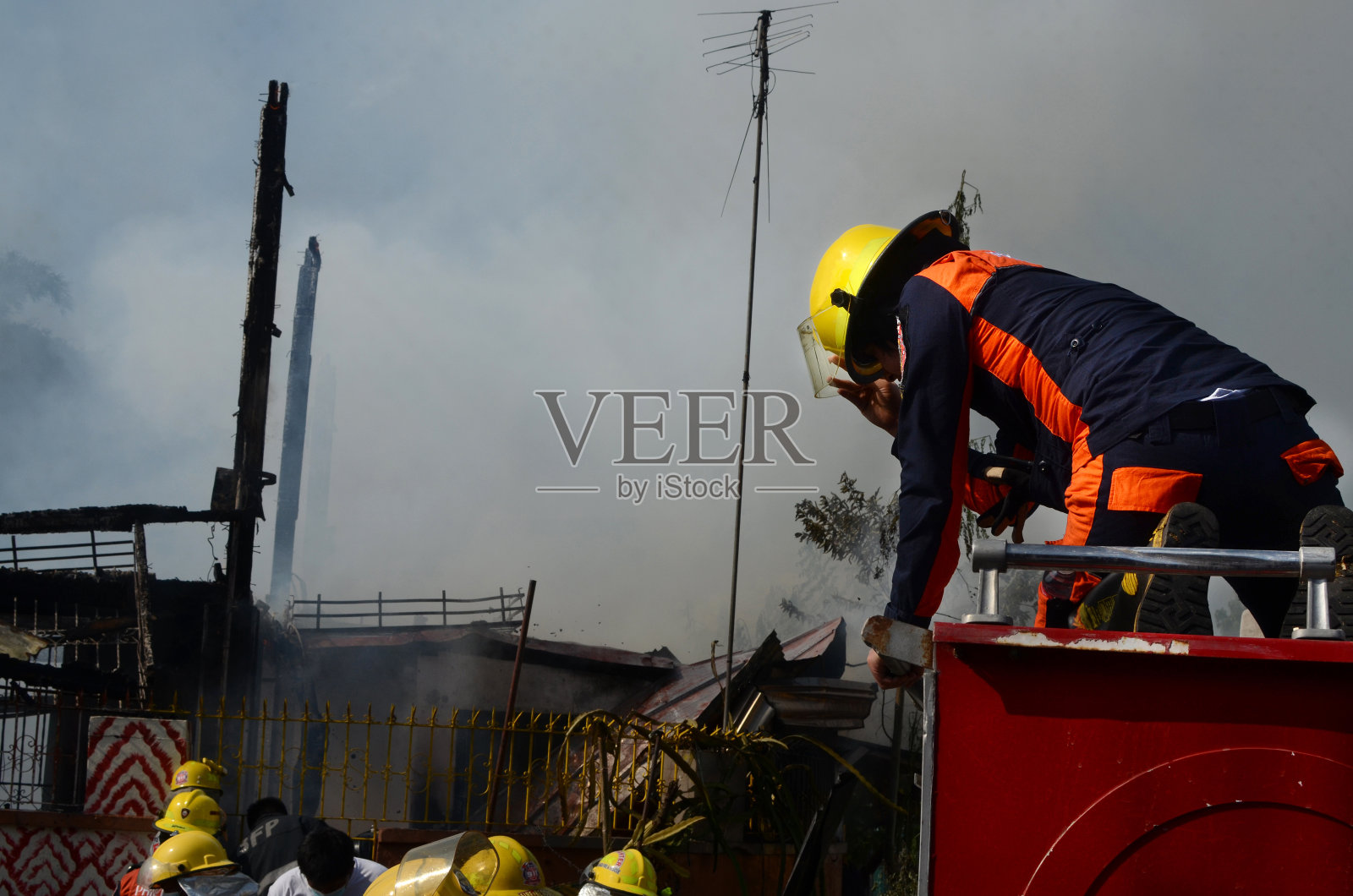戴着防护帽的女消防队员爬上着火的房子的消防车顶部照片摄影图片