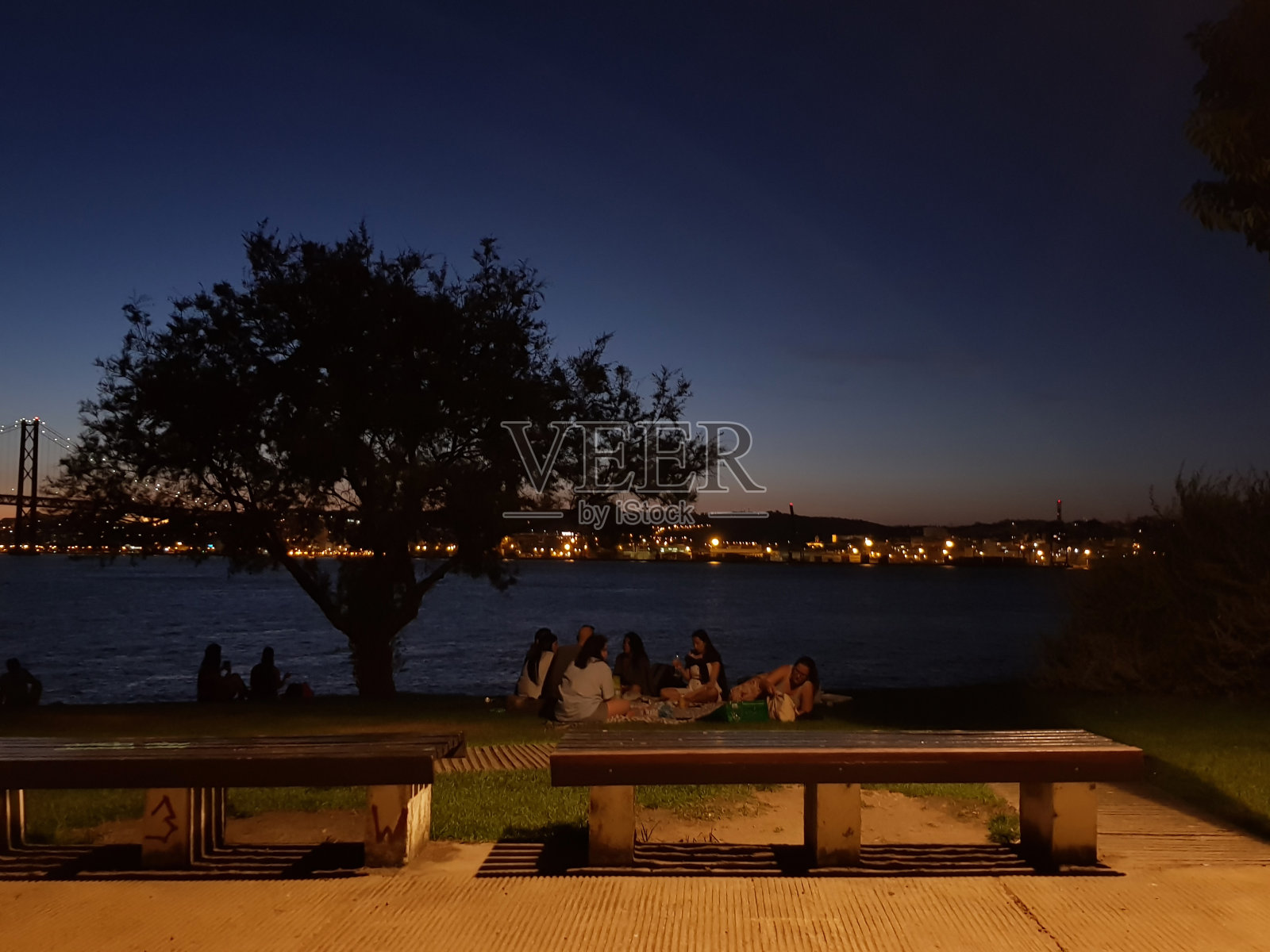 黄昏时分，人们以城市的灯光为背景，在河边放松照片摄影图片