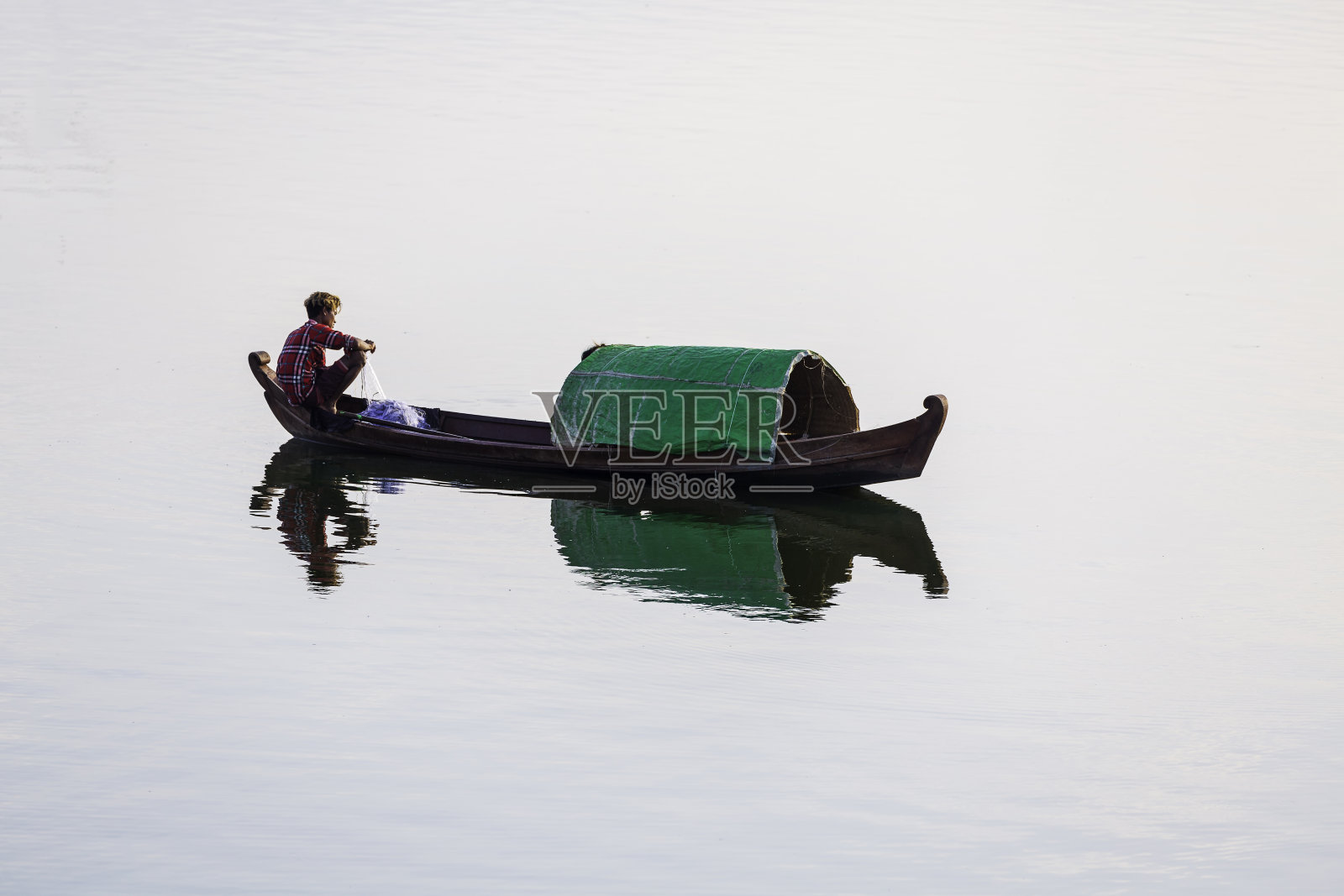一位缅甸渔民坐在一艘木制渔船上，用渔网将鱼困在湖中。照片摄影图片
