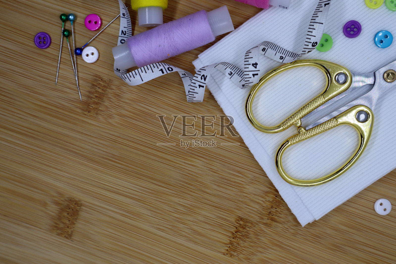 木制背景上的一套缝纫配件。布料、线、厘米和剪刀。照片摄影图片
