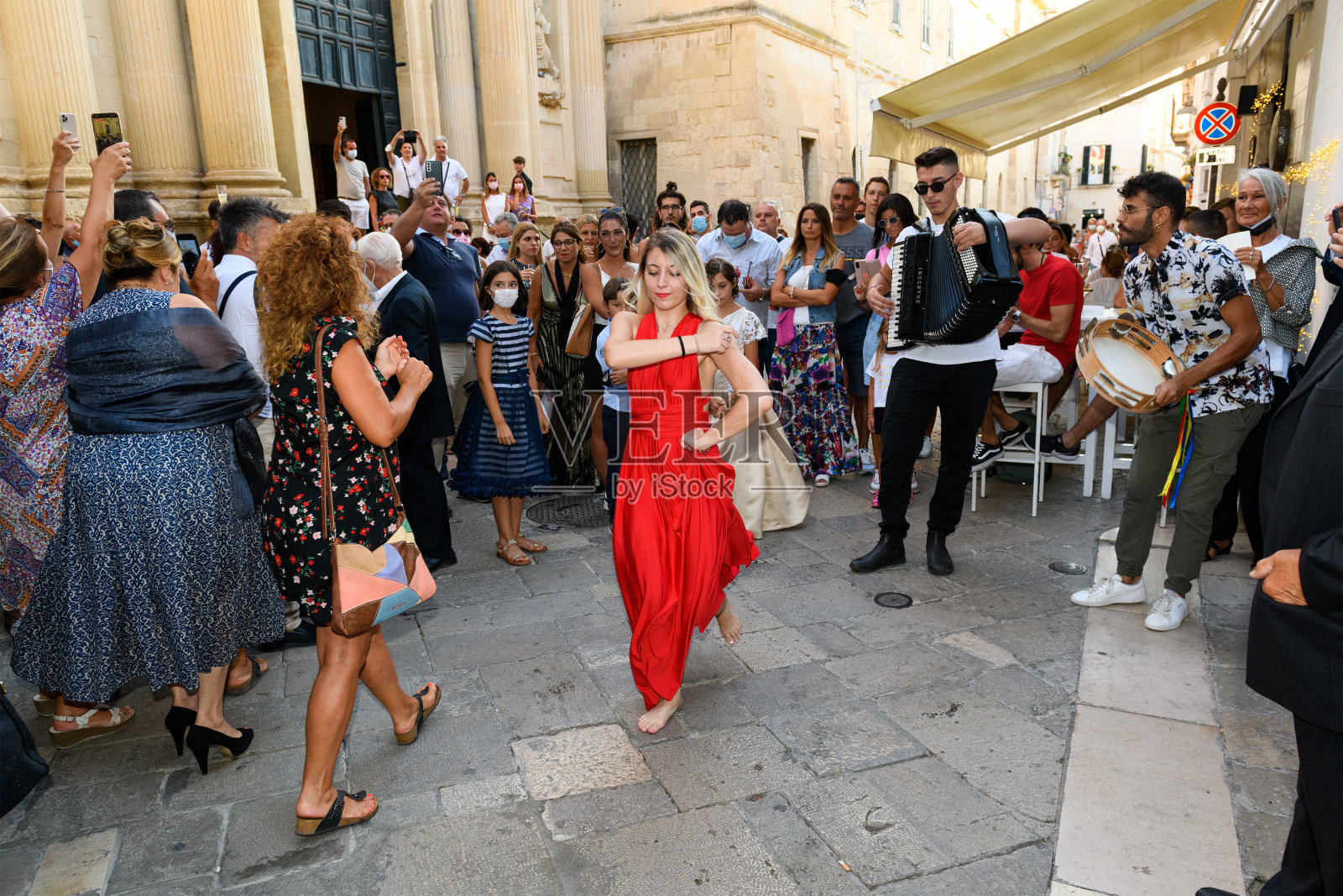 莱切的夏日街道上,一名穿着红色连衣裙的女子赤脚跳着一种叫pizzica或taranta的阿普利亚民间舞蹈照片摄影图片