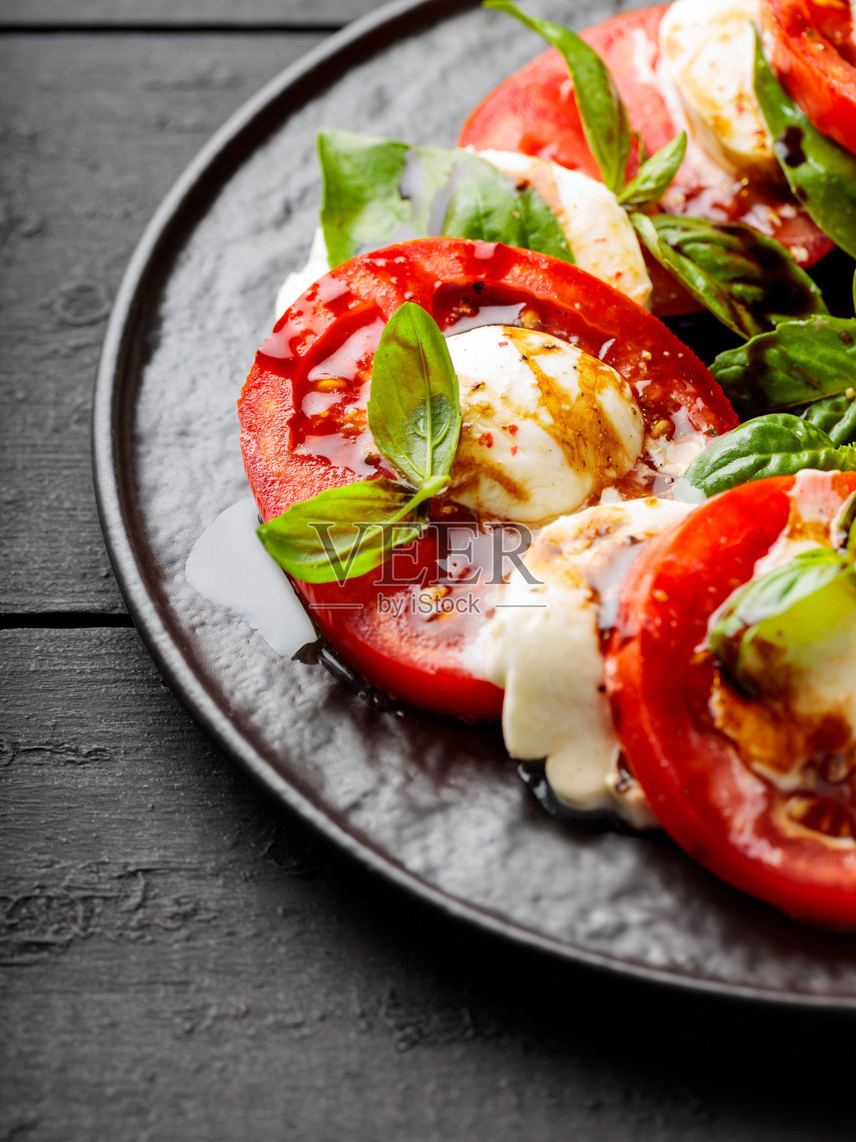 美味的卡普里斯沙拉配上成熟的西红柿、马苏里拉奶酪和新鲜的罗勒叶，放在深色的木板上。近距离照片摄影图片