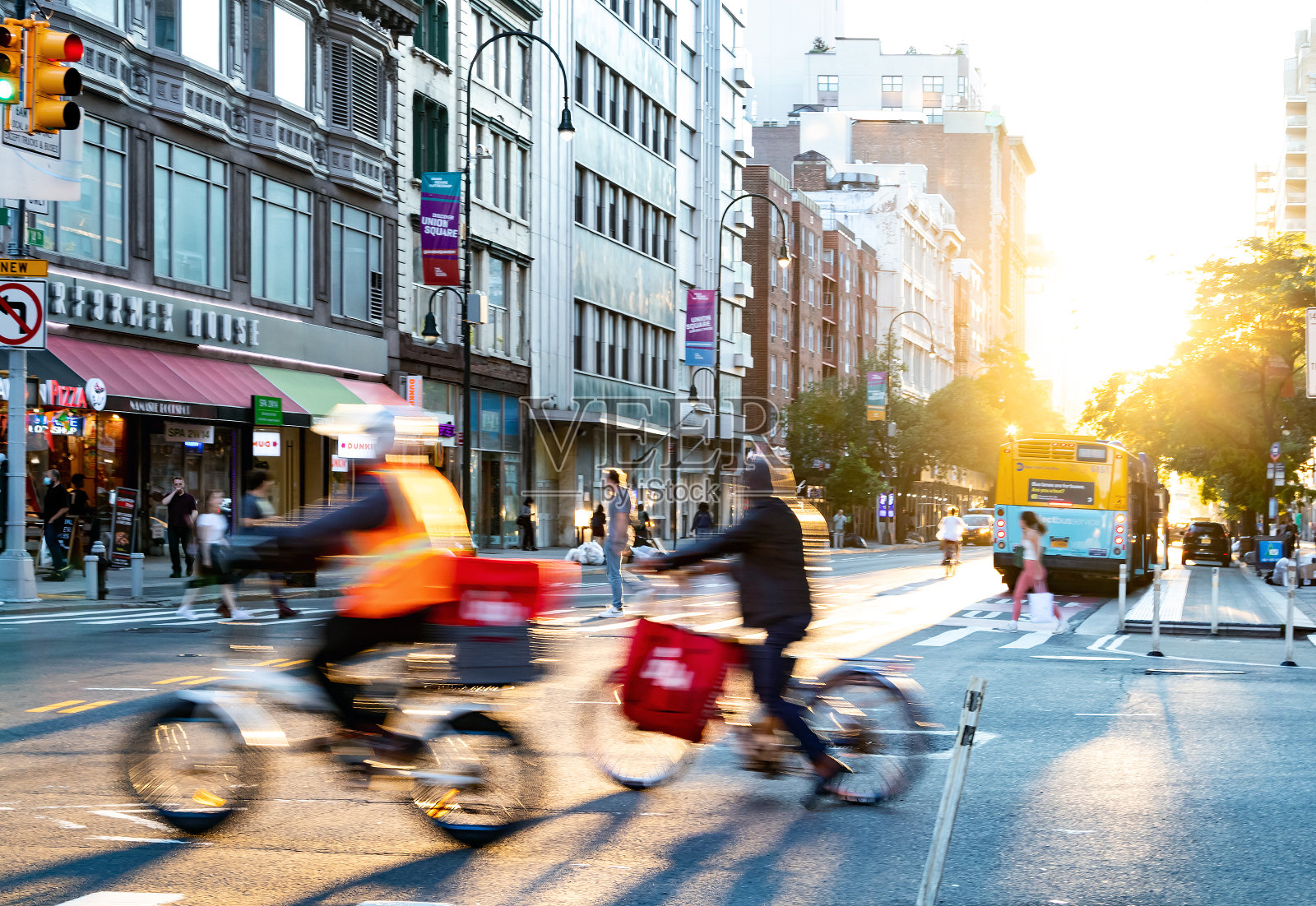 纽约市——在夕阳的背景下，骑着自行车送快递的人穿过第14街和第5大道的繁忙十字路口照片摄影图片