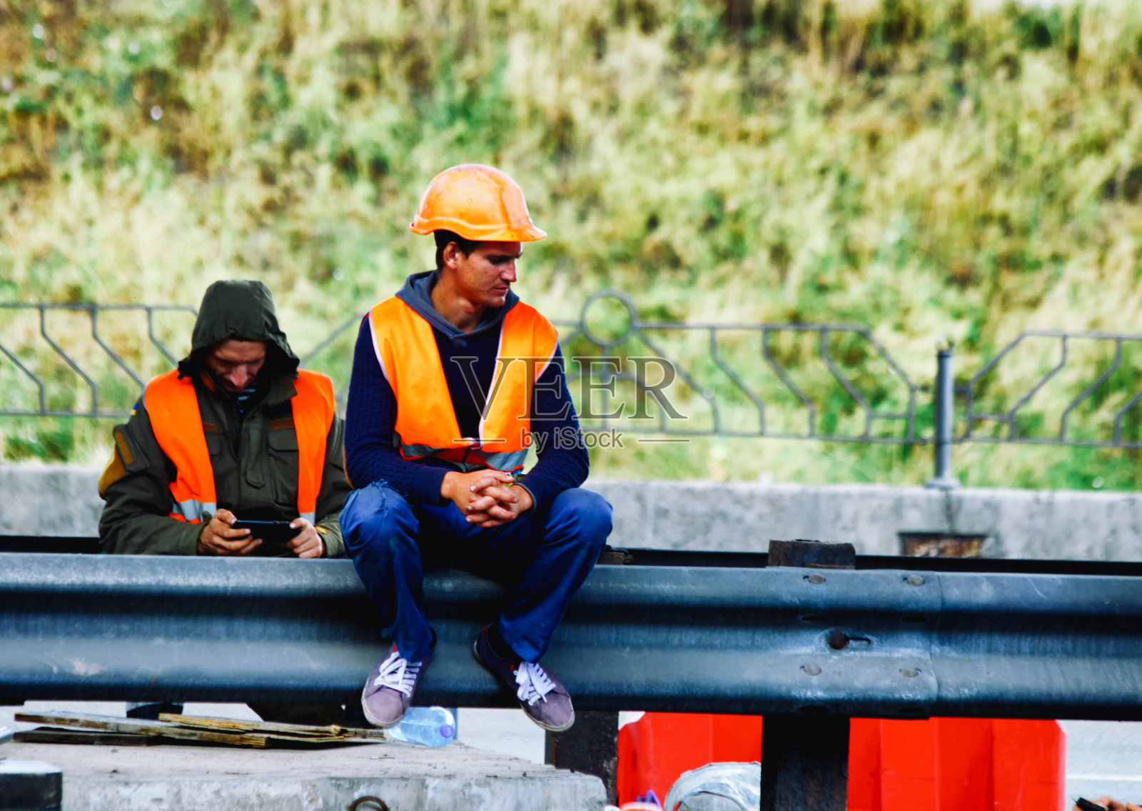 修路工人，一个在展望未来，一个在看智能手机照片摄影图片