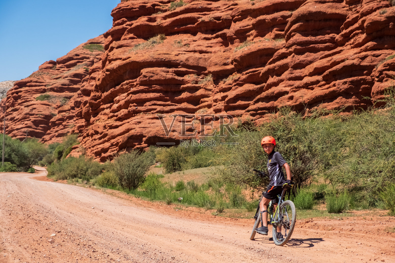 年轻的自行车手在碎石路上与红色侵蚀的山脉背景。休闲、旅游、休闲理念。照片摄影图片