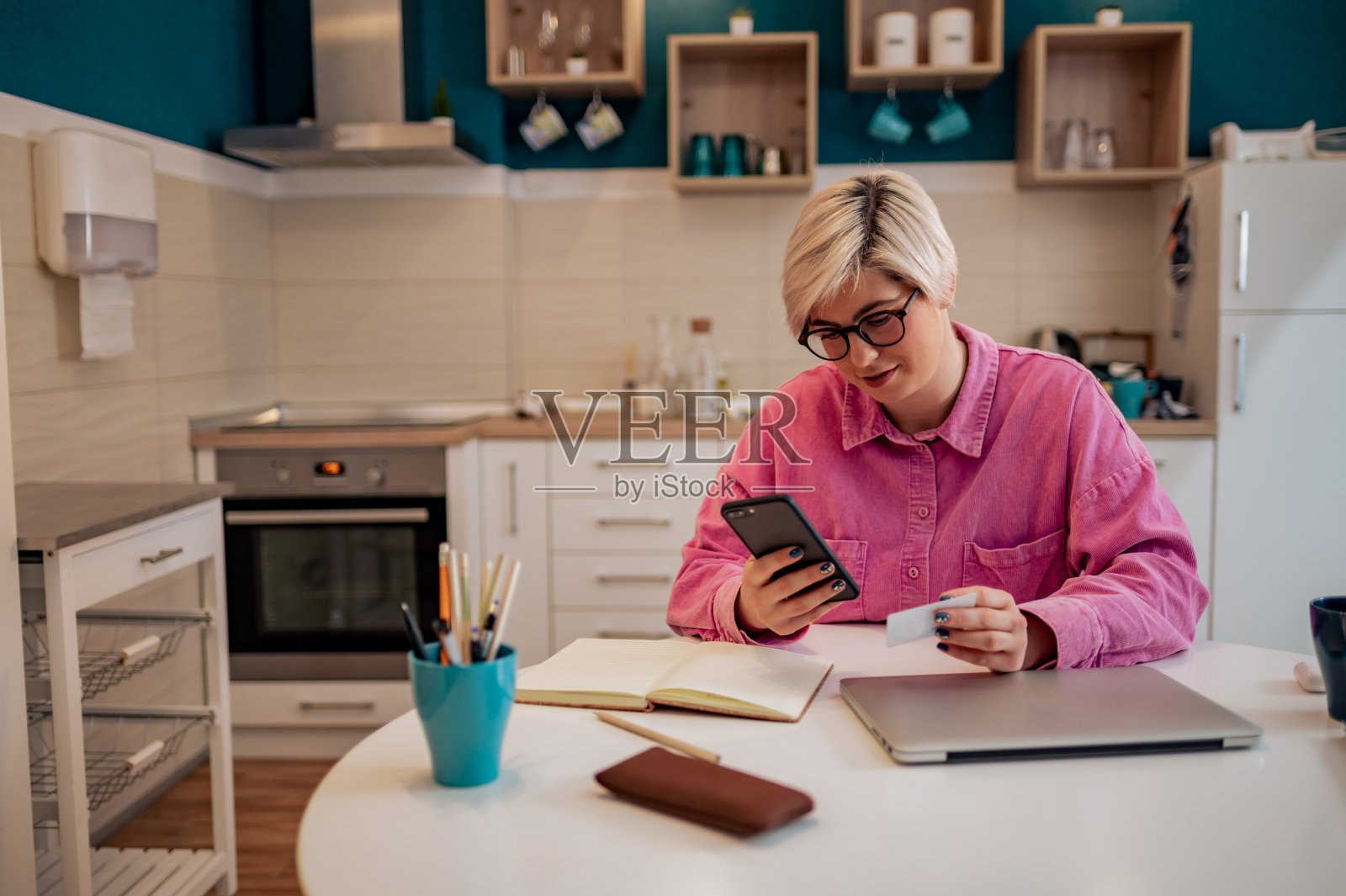 金发短发的女人拿着信用卡，在家里用智能手机照片摄影图片