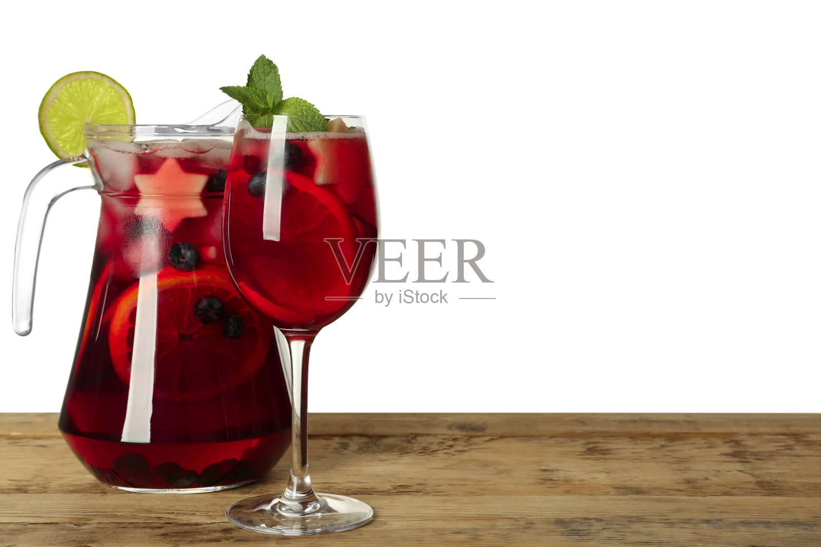 白色背景的木制桌子上的玻璃和红色桑格里亚汽酒壶。空间的文本照片摄影图片