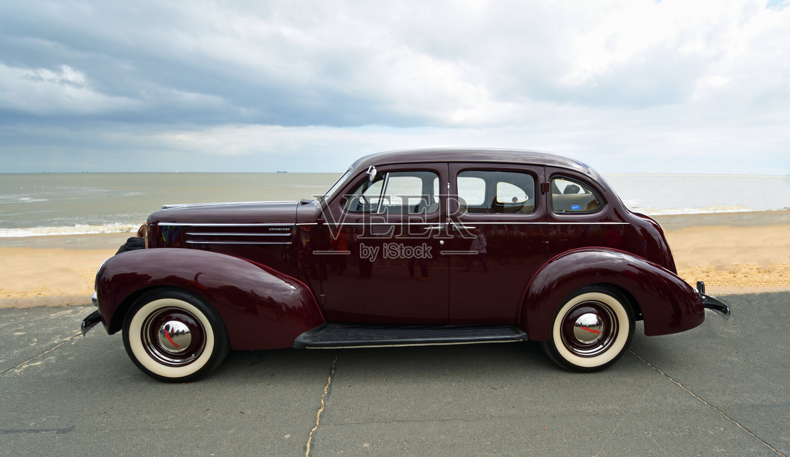 经典的深红色斯图贝克汽车停在海滨长廊海滩和大海的背景。照片摄影图片