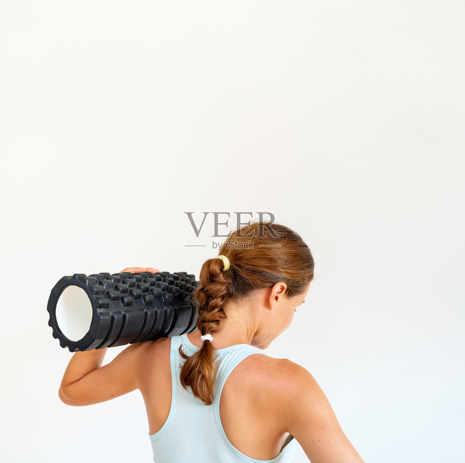 健身的概念照片，后视图的年轻运动员妇女穿着运动胸罩抱泡沫辊在她的肩膀上。照片摄影图片