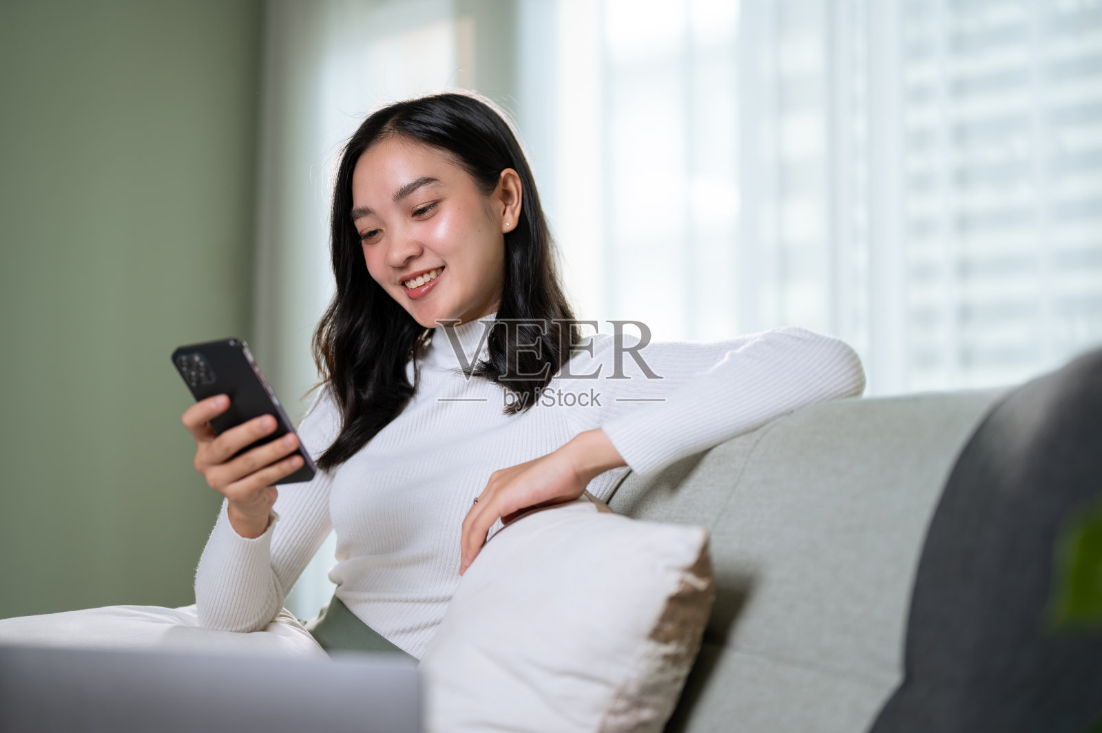 一个美丽的亚洲女人喜欢在网上购物，在沙发上放松地阅读网上博客照片摄影图片