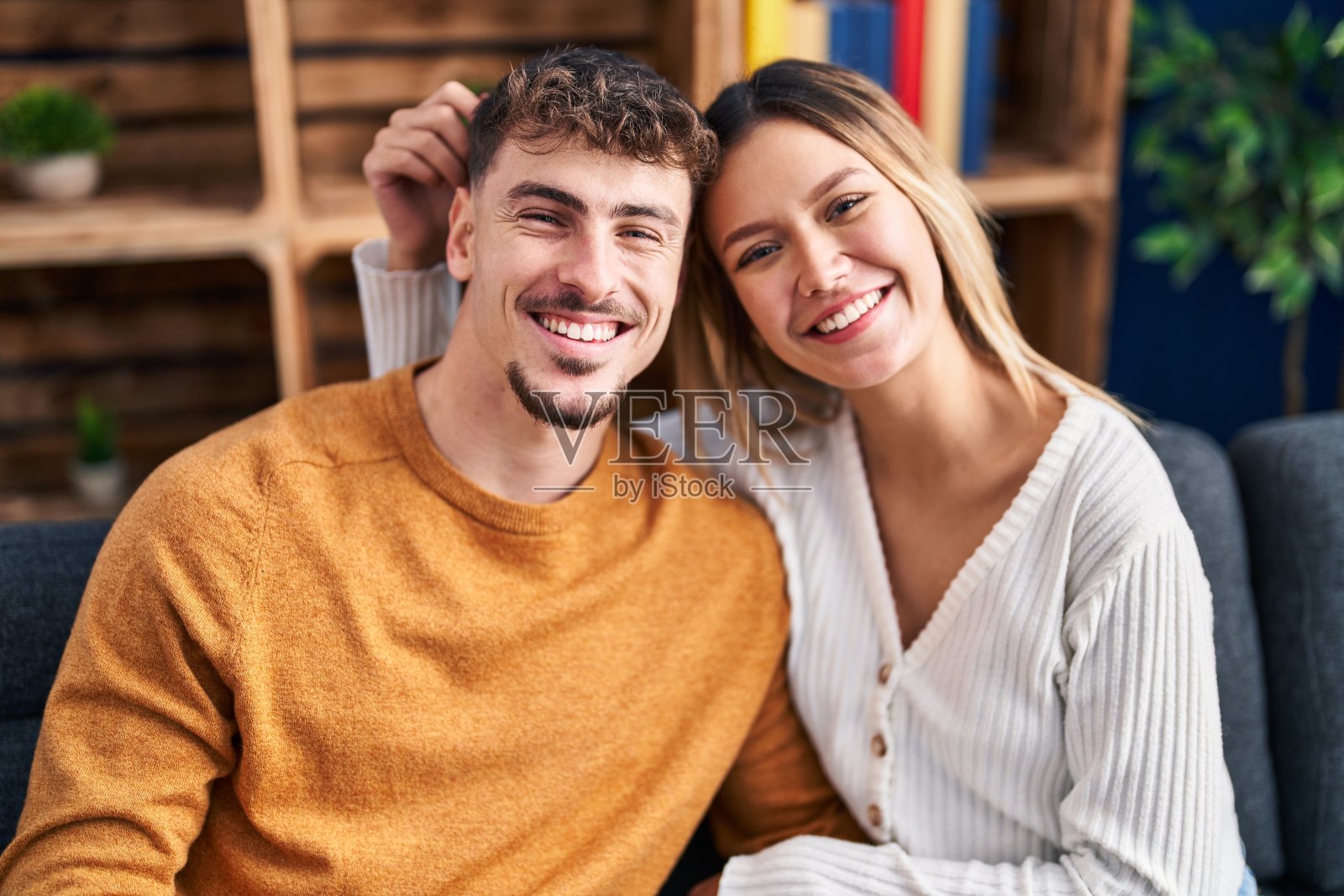 年轻的男女夫妇拥抱在一起坐在家里的沙发上照片摄影图片