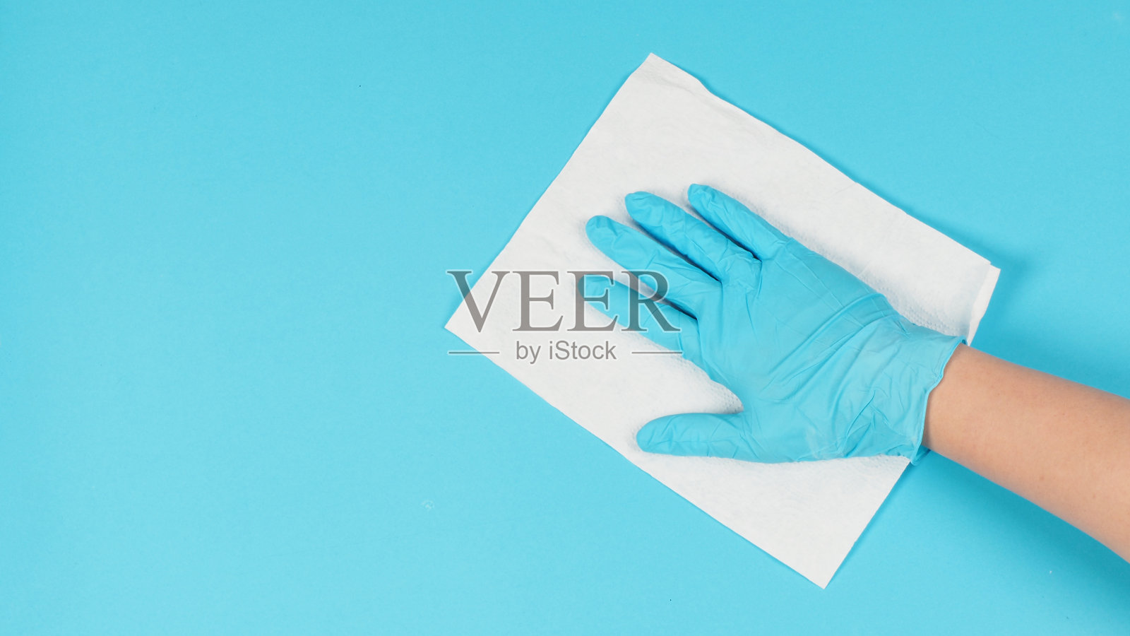 手在蓝色背景上擦拭并握住白色纸巾。手戴蓝色乳胶手套。照片摄影图片