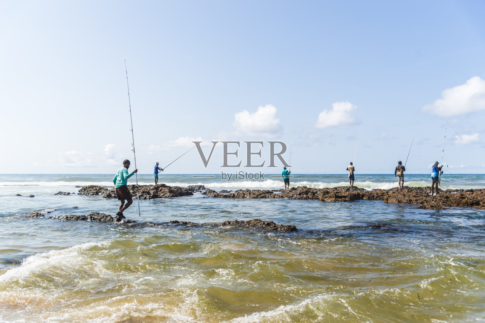 渔民在海滩岩石上用钓竿钓鱼照片摄影图片