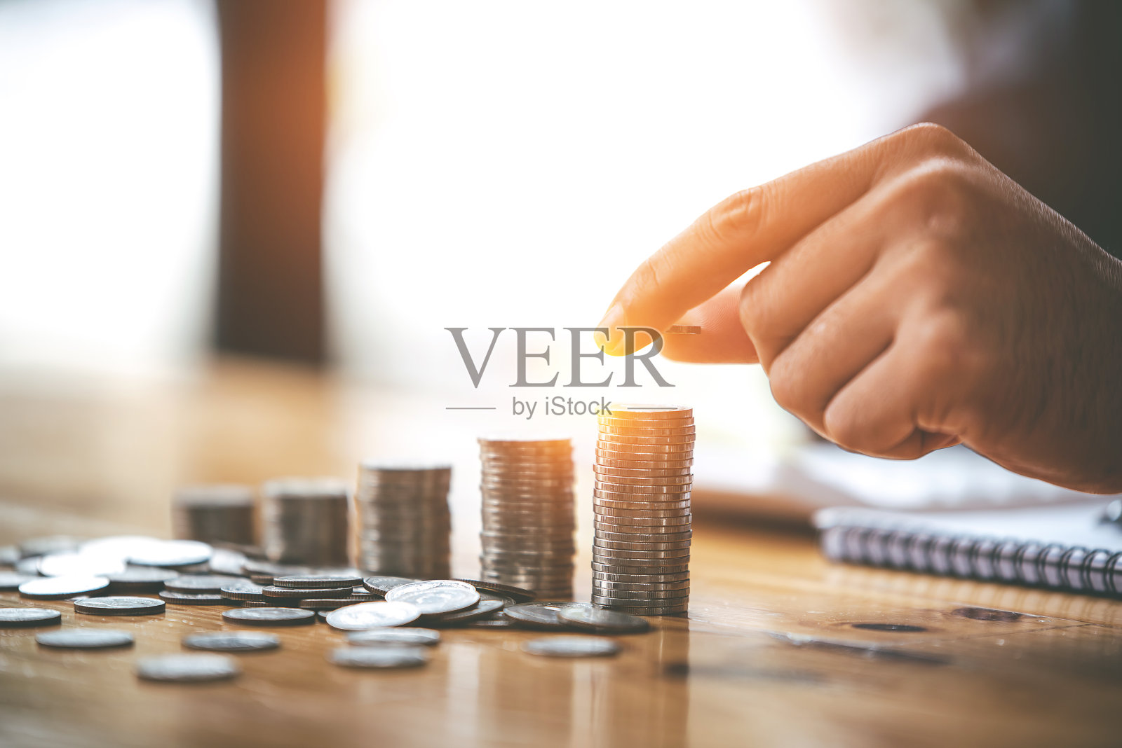 拿着省钱硬币，把硬币放在有阳光的桌子上。财务会计概念照片摄影图片