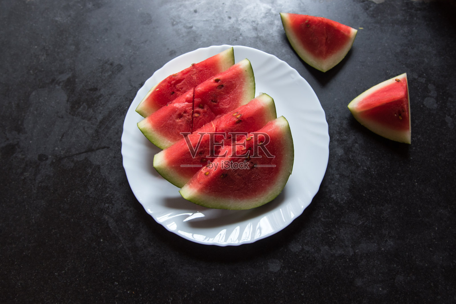 健康的水果在黑色背景的白色盘子里切成片的西瓜。照片摄影图片