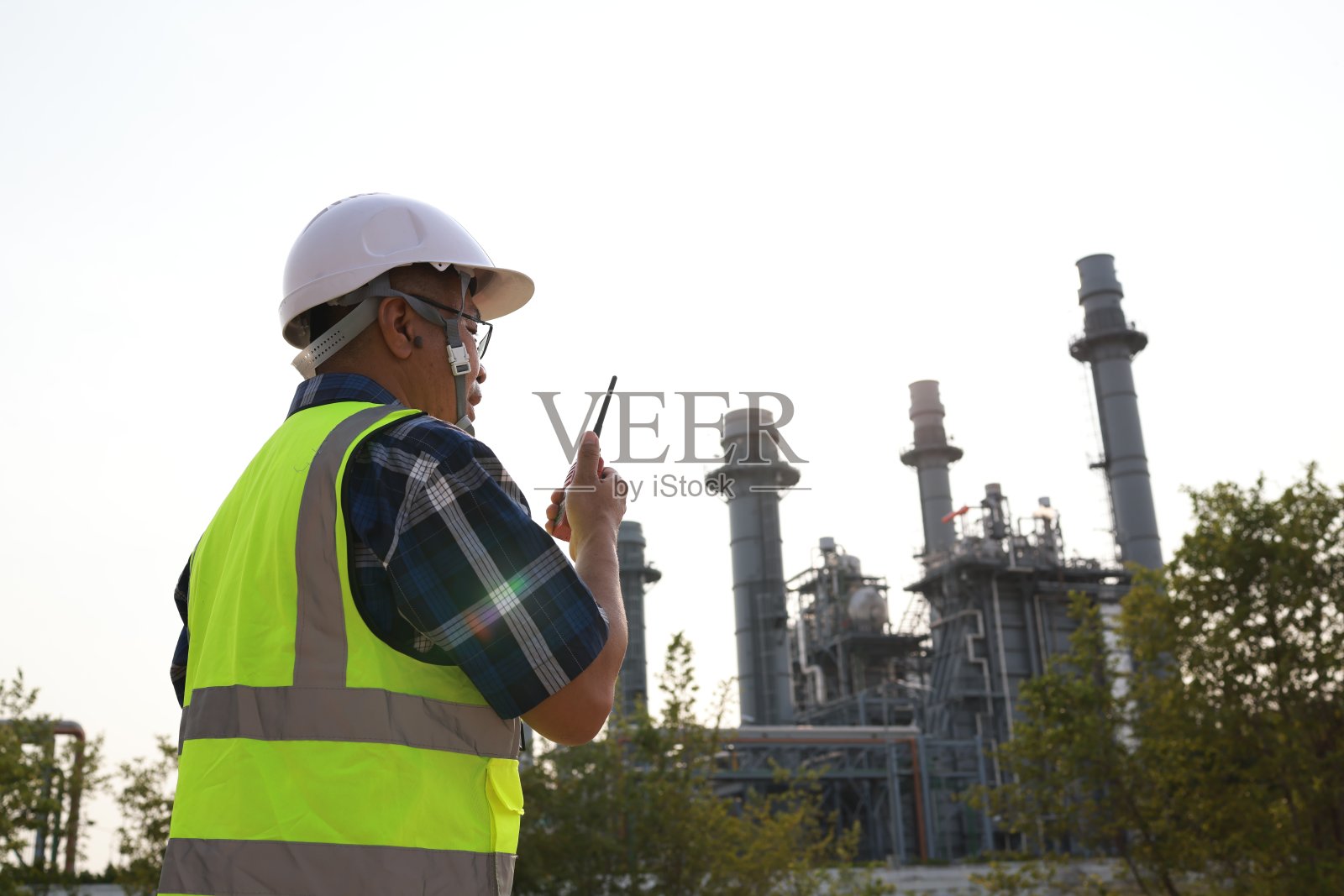 高级工程师穿着安全背心，戴安全帽，站在电厂，工厂和工程概念前通过对讲机与团队沟通照片摄影图片