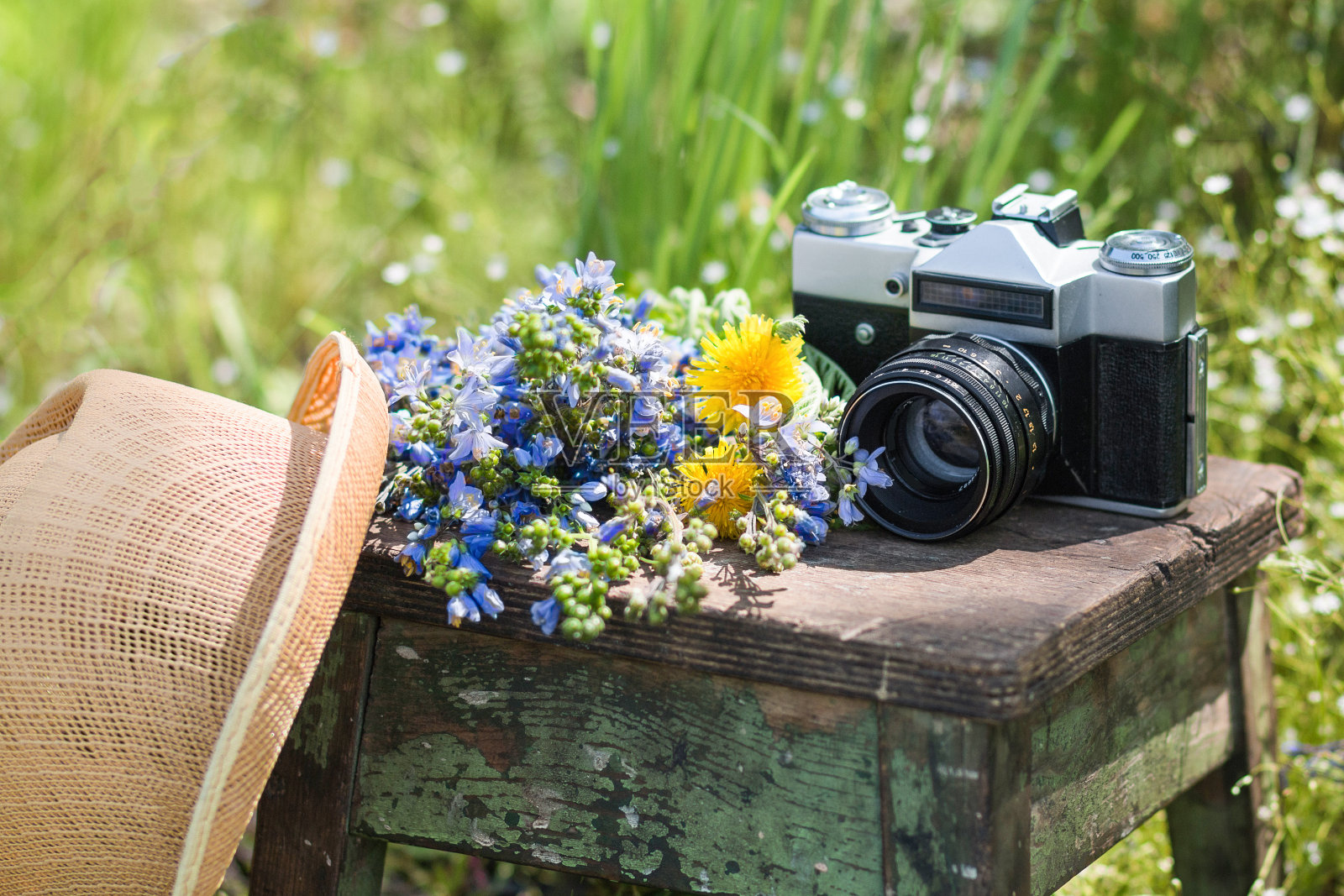 夏天花园里的木椅上放着草帽、野花和复古胶卷相机。照片摄影图片