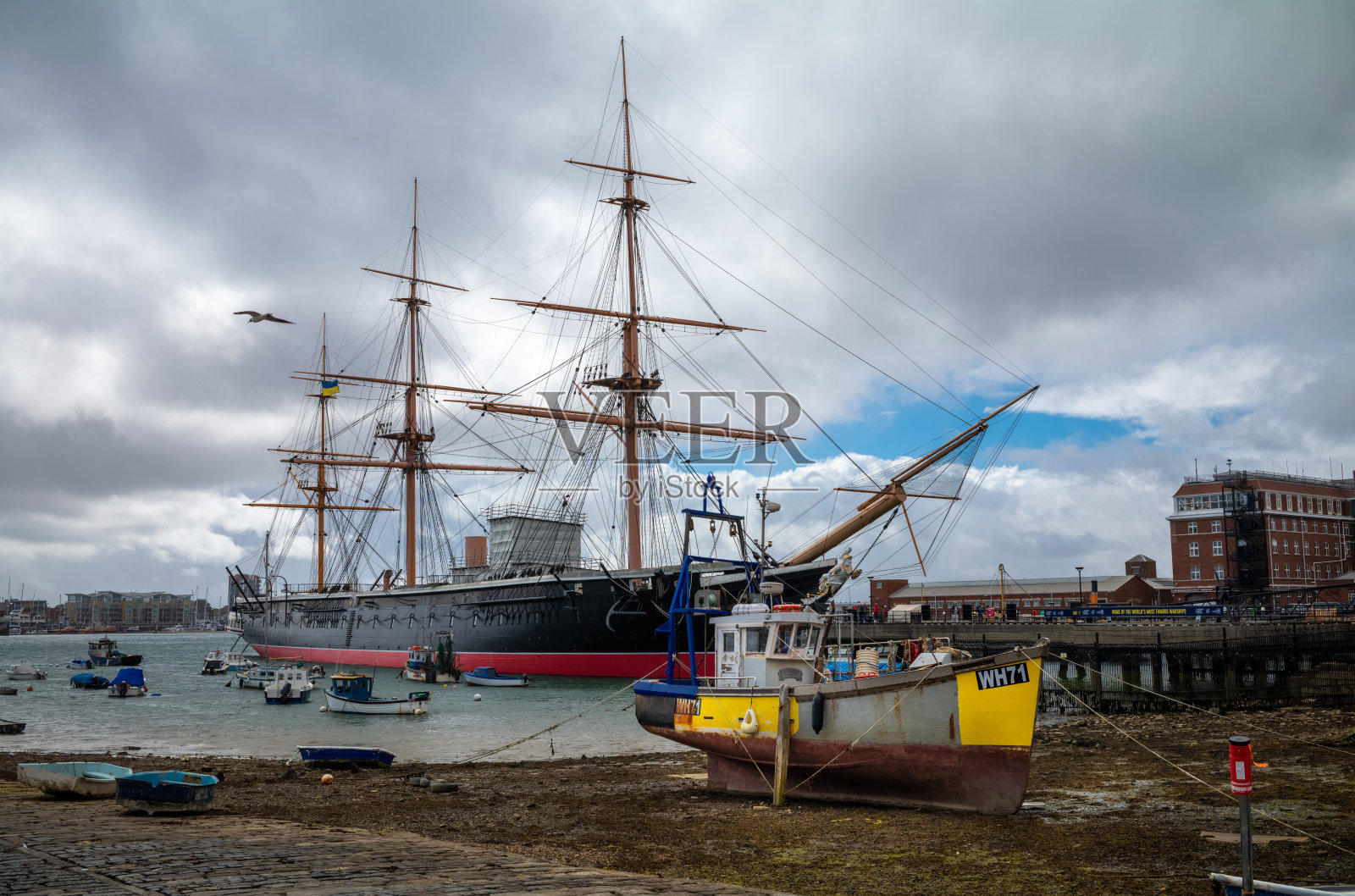 在英国朴茨茅斯，一艘被称为La Serime的废弃渔船在退潮时停靠在历史悠久的战舰HMS Warrior前照片摄影图片