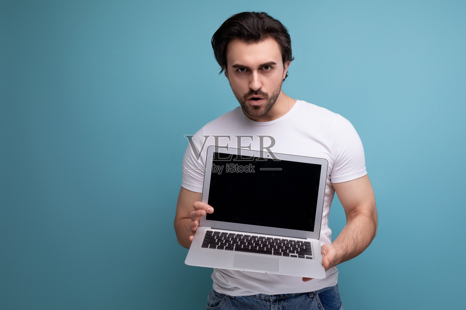 留着胡子的黑发男子，穿着白色背心，手提电脑放在工作室背景上，上面有文案照片摄影图片