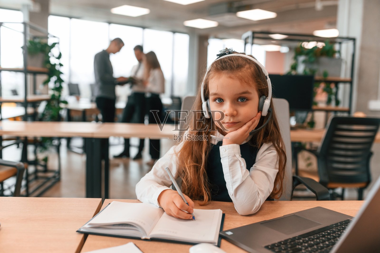 笔记本电脑在桌子上。小女孩在办公室里，人们一起工作照片摄影图片