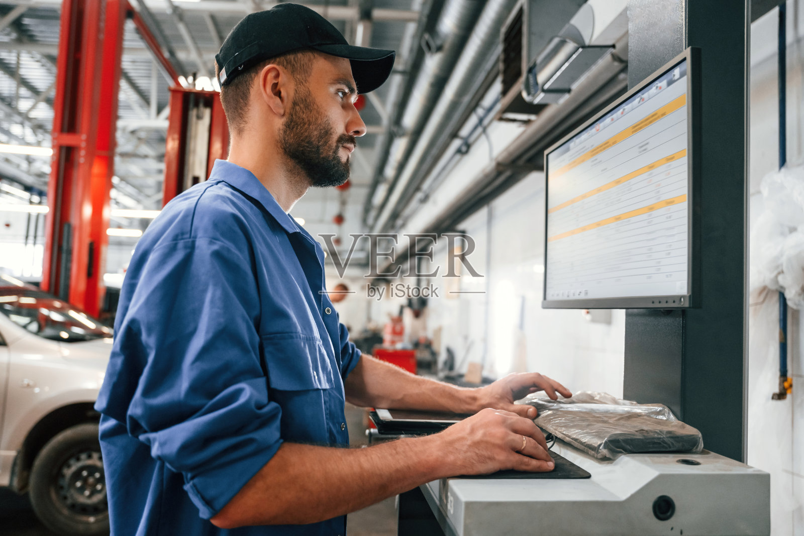 侧视图，使用电脑。汽车修理工在汽车修理厂工作。维修服务照片摄影图片