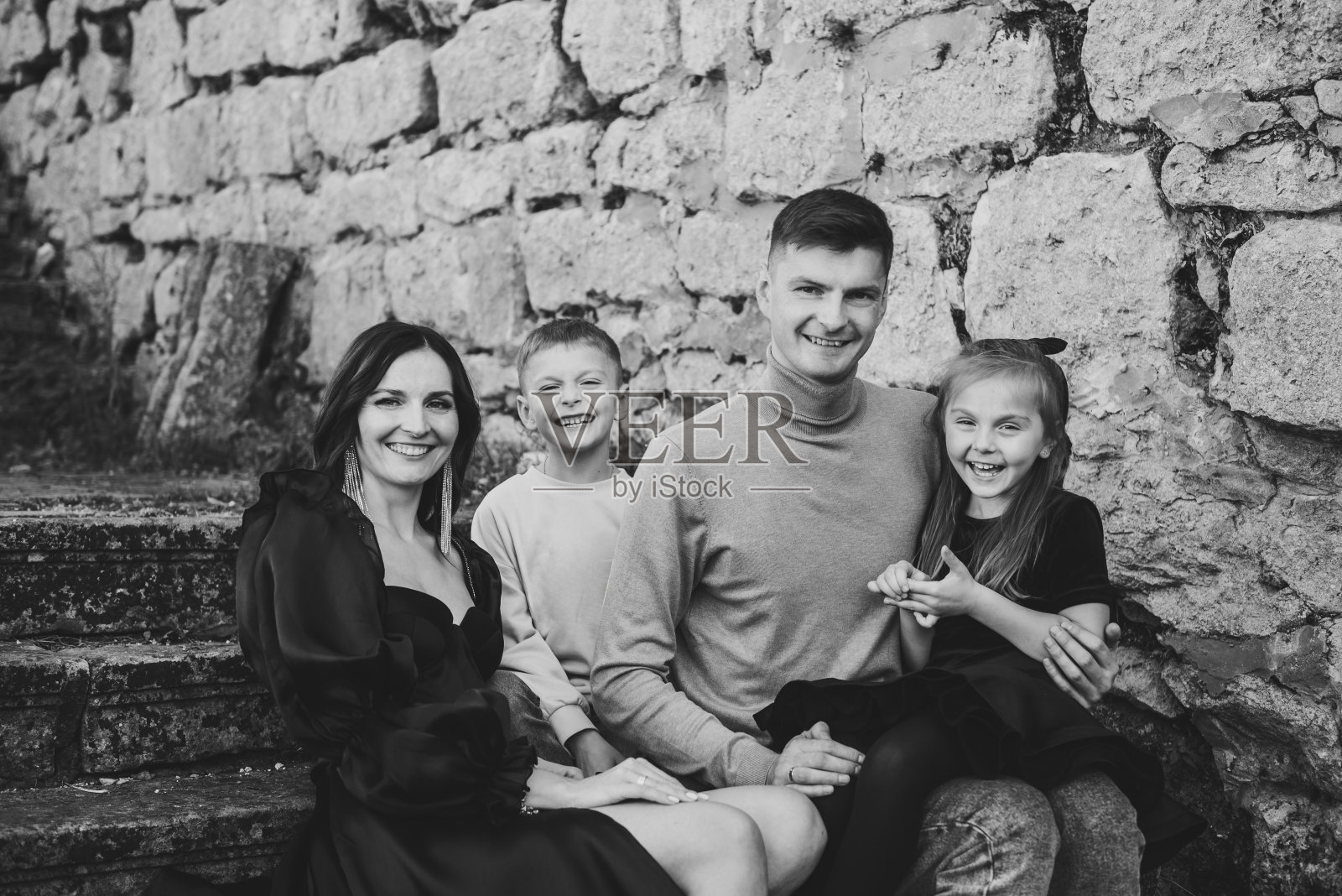 母亲，父亲，女儿，儿子坐在古代宫殿附近的楼梯上。妈妈，爸爸在大自然中拥抱快乐的孩子们。孩子们在老砖墙旁拥抱父母。家人聚在一起。黑白照片照片摄影图片