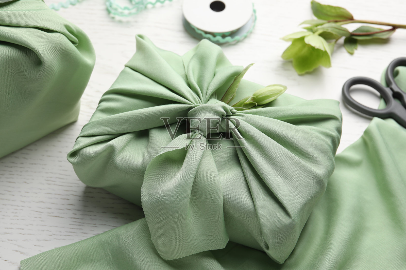 Furoshiki技术。礼品包装在绿色织物和白色木桌上装饰有嚏根草花，特写照片摄影图片