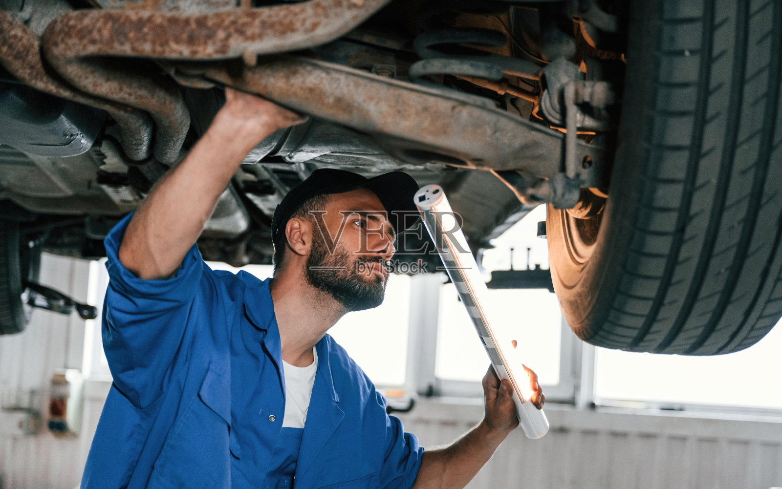 站在汽车下面。汽车修理工在汽车修理厂工作。维修服务照片摄影图片