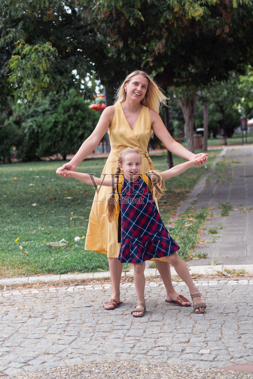 年轻的女学生和她的妈妈的肖像，愉快地跳跃与母亲公园在上学的路上。照片摄影图片