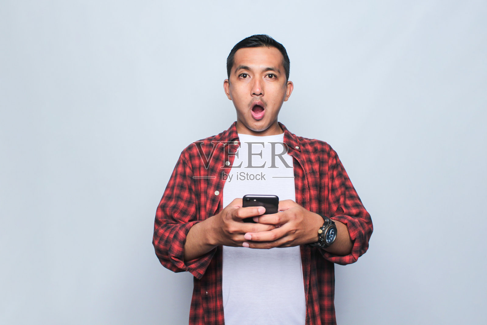 一个年轻的亚洲男子用智能手机在白色背景上微笑的工作室照片。照片摄影图片