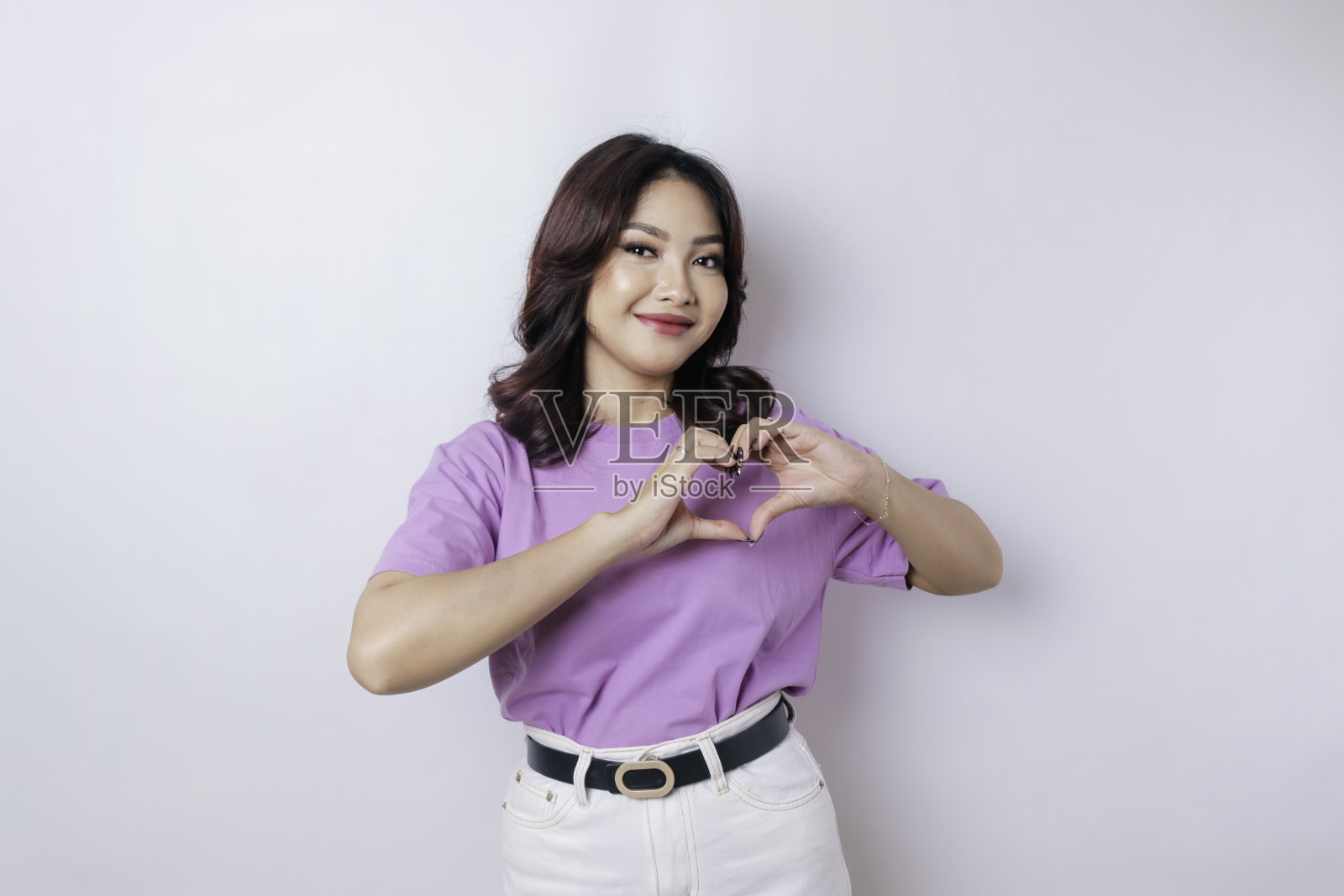 一个迷人的年轻亚洲女人穿着淡紫色的t恤感到快乐，一个浪漫的心形手势表达了温柔的感情照片摄影图片