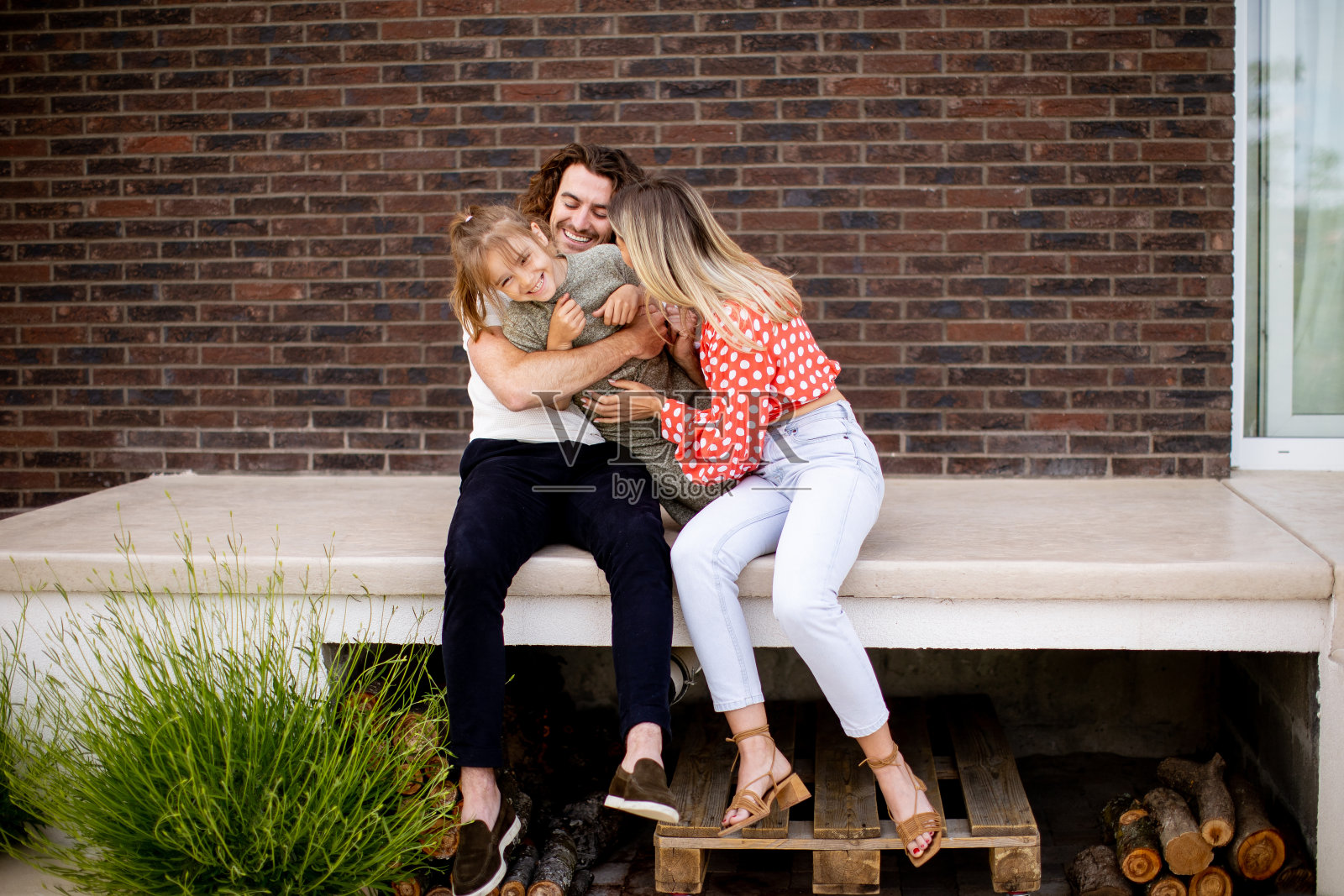 一家人，父亲、母亲和女儿坐在砖房前廊的台阶上照片摄影图片