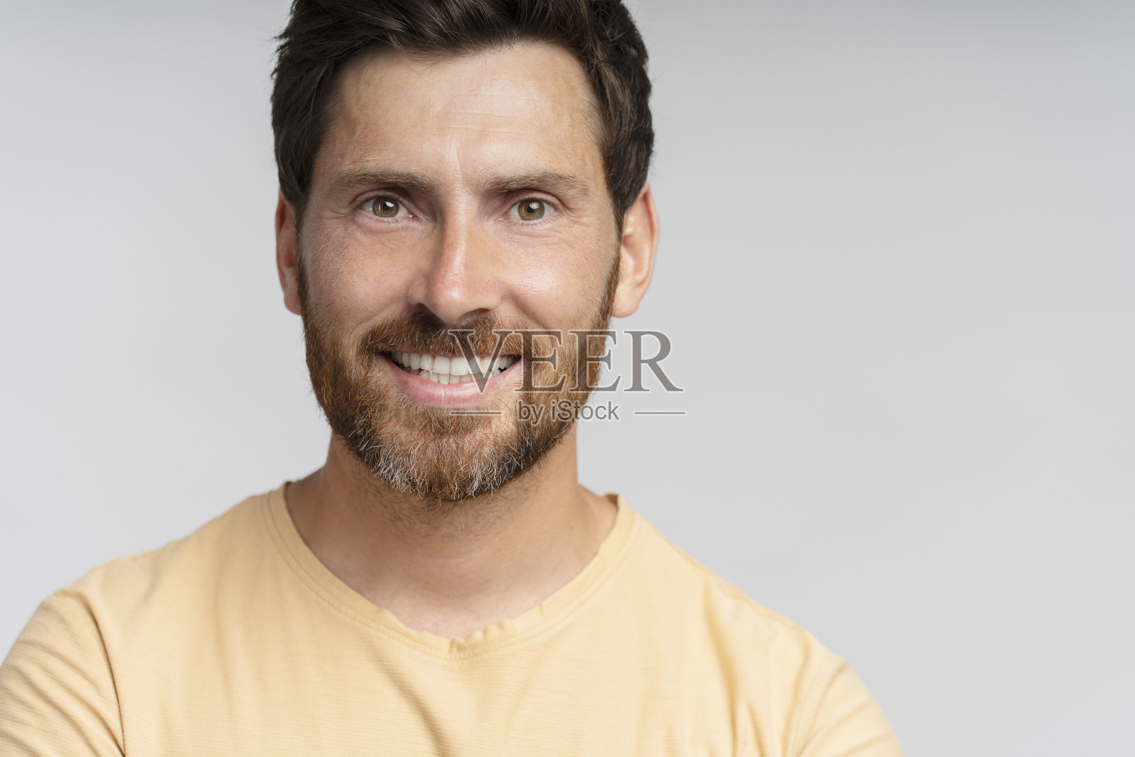 在灰色的背景上，一个面带微笑的留着胡子的中年男子看着相机照片摄影图片