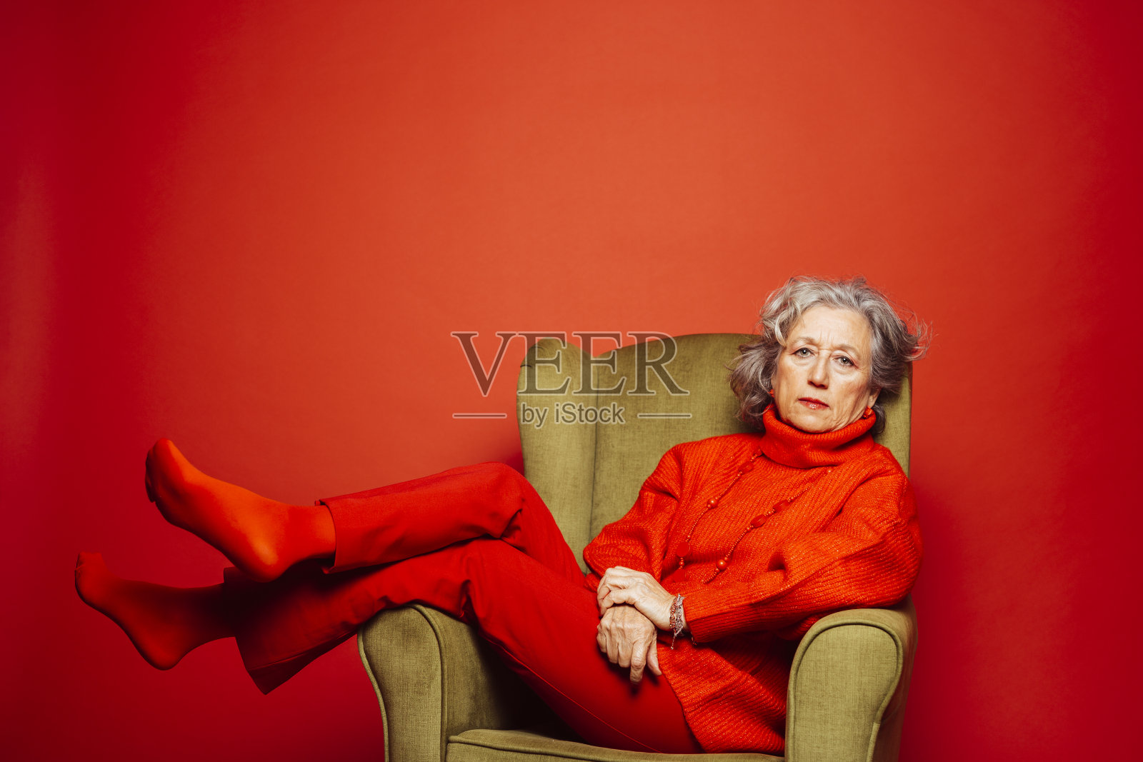 一位年长的女士躺在扶手椅上，前面是红色的背景照片摄影图片