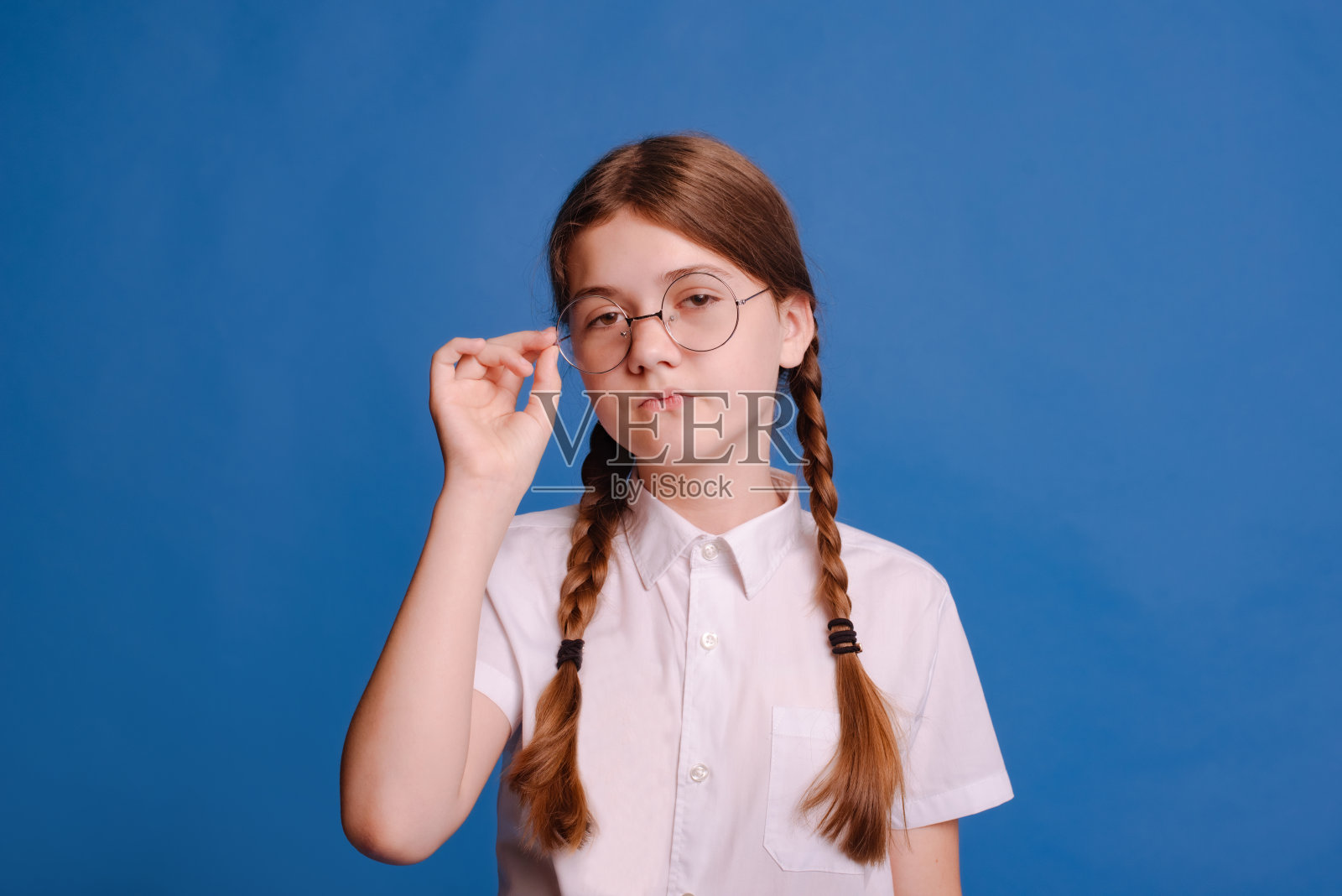 严肃的女学生戴着矫正视力的圆眼镜，看着蓝色摄影棚背景上的照相机照片摄影图片