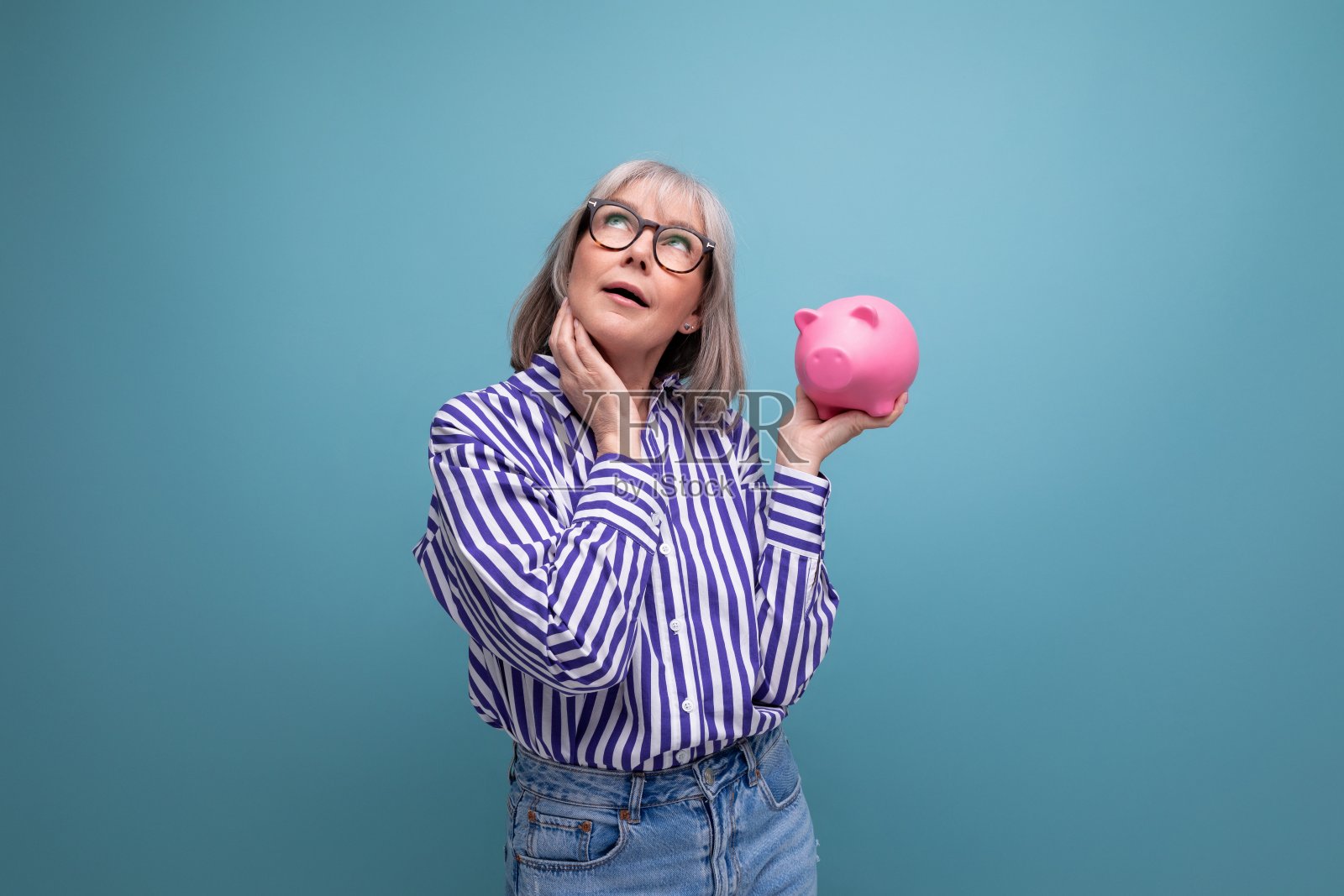 沉思的60多岁的白发女人拿着存钱罐在明亮的工作室背景下思考保险问题照片摄影图片